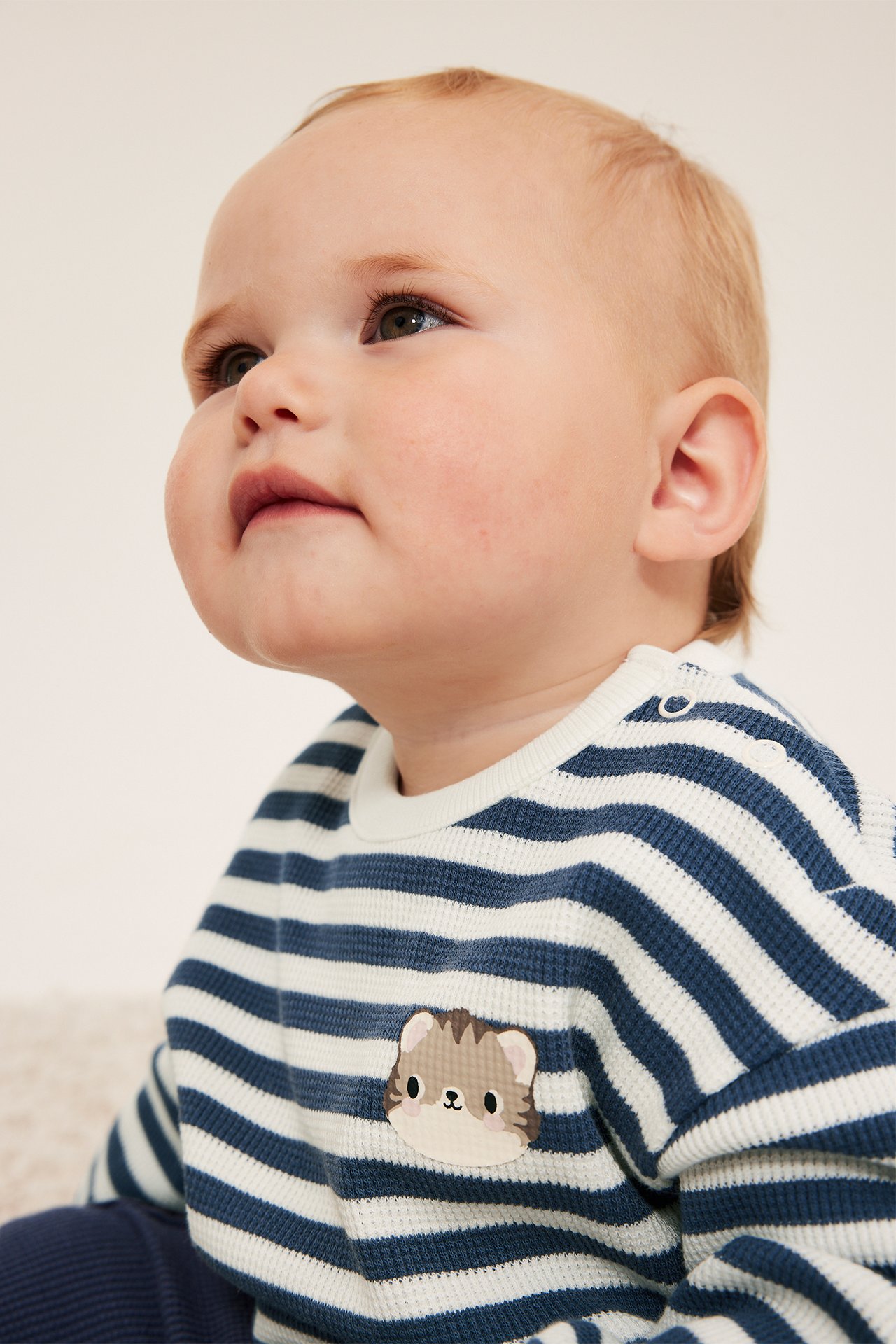 Närbild på baby i blåvitrandig våffelstickad tröja med djurlapp och mörkblå byxor.