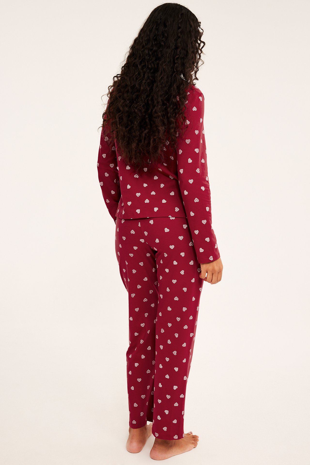 Nainen selin, yllään viininpunainen pitkähihainen sydänkuvioinen pyjama.
