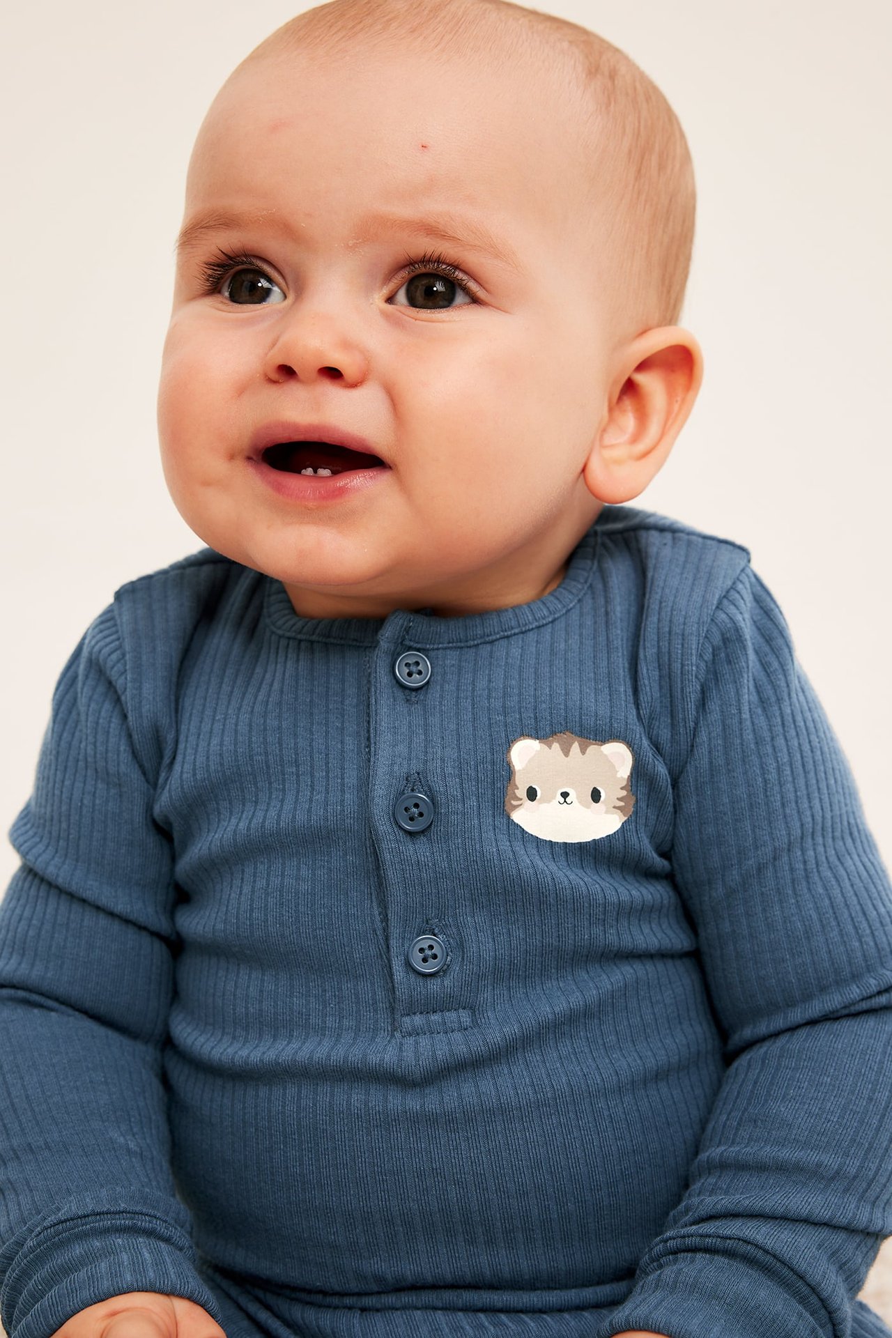 Zbliżenie na dziecko w niebieskim, prążkowanym body Henley z długim rękawem z naszywką kotka.