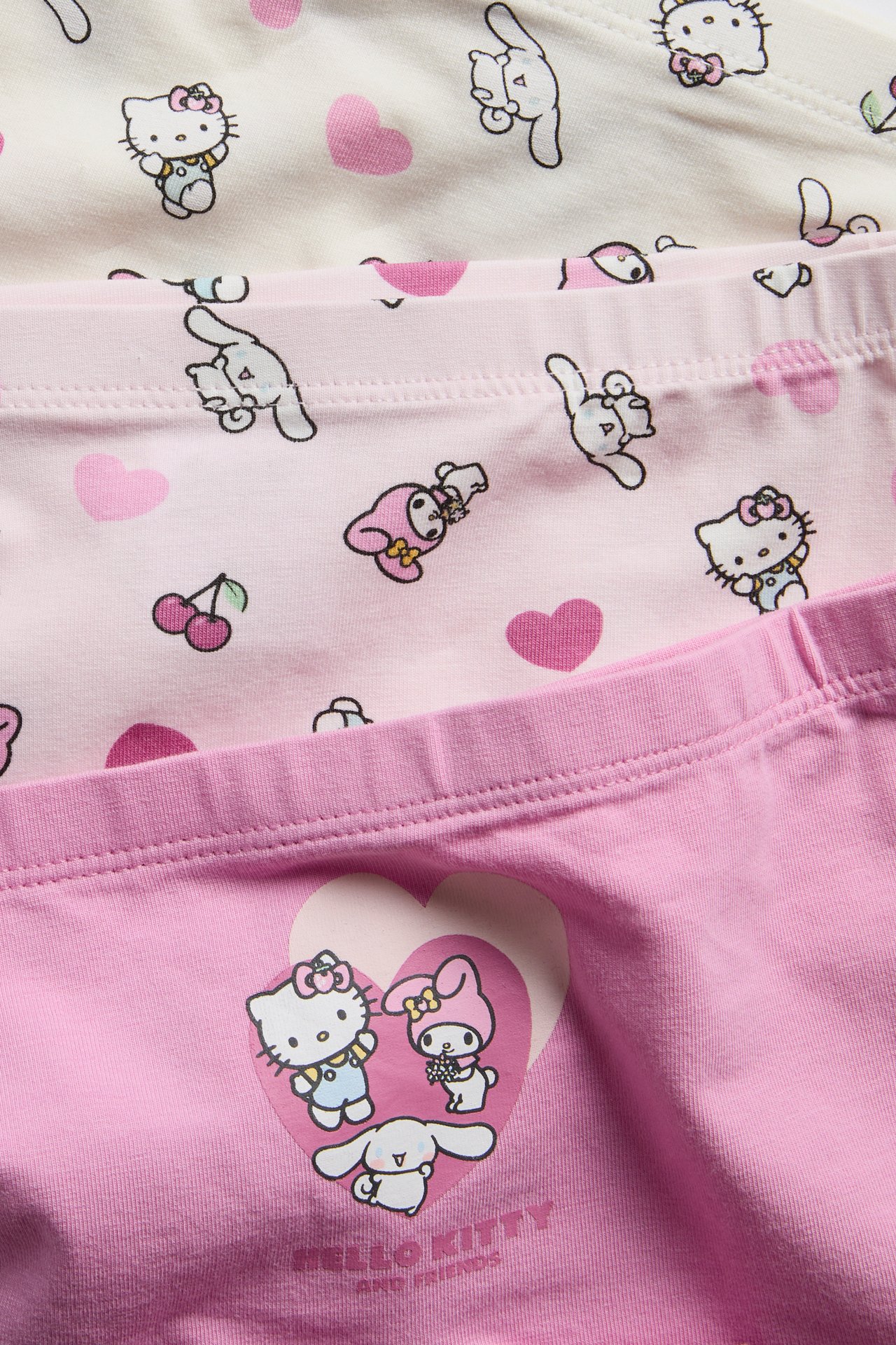 Zbliżenie na trzy pary różowo-białych majtek dziecięcych z nadrukiem Hello Kitty i przyjaciół.