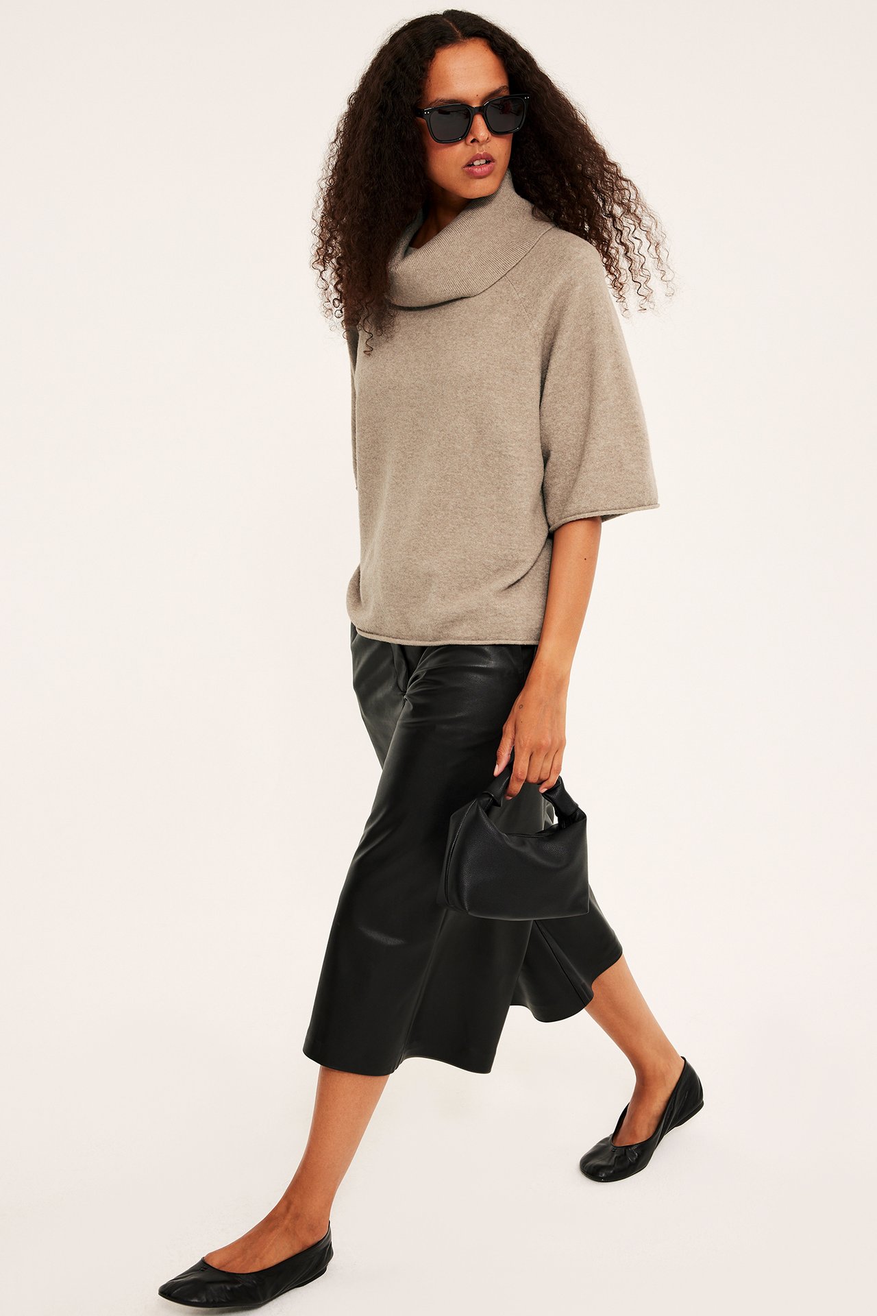 Framifrån: Kvinna i beige polotröja, svarta läderculottes, svarta ballerinaskor, med svart handväska.