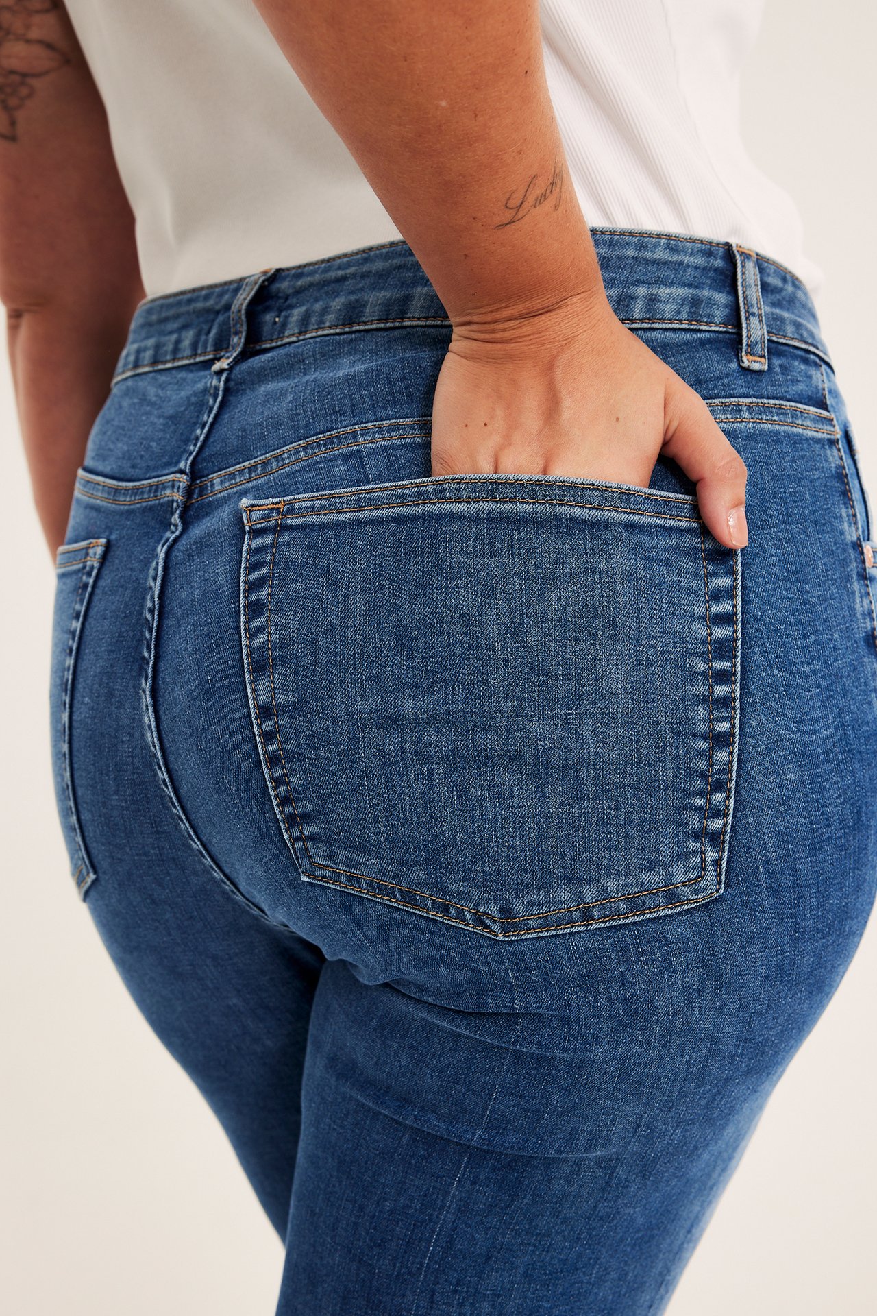 Nærbilde bakfra av en kvinne i blå tettsittende jeans med en hånd i baklommen.