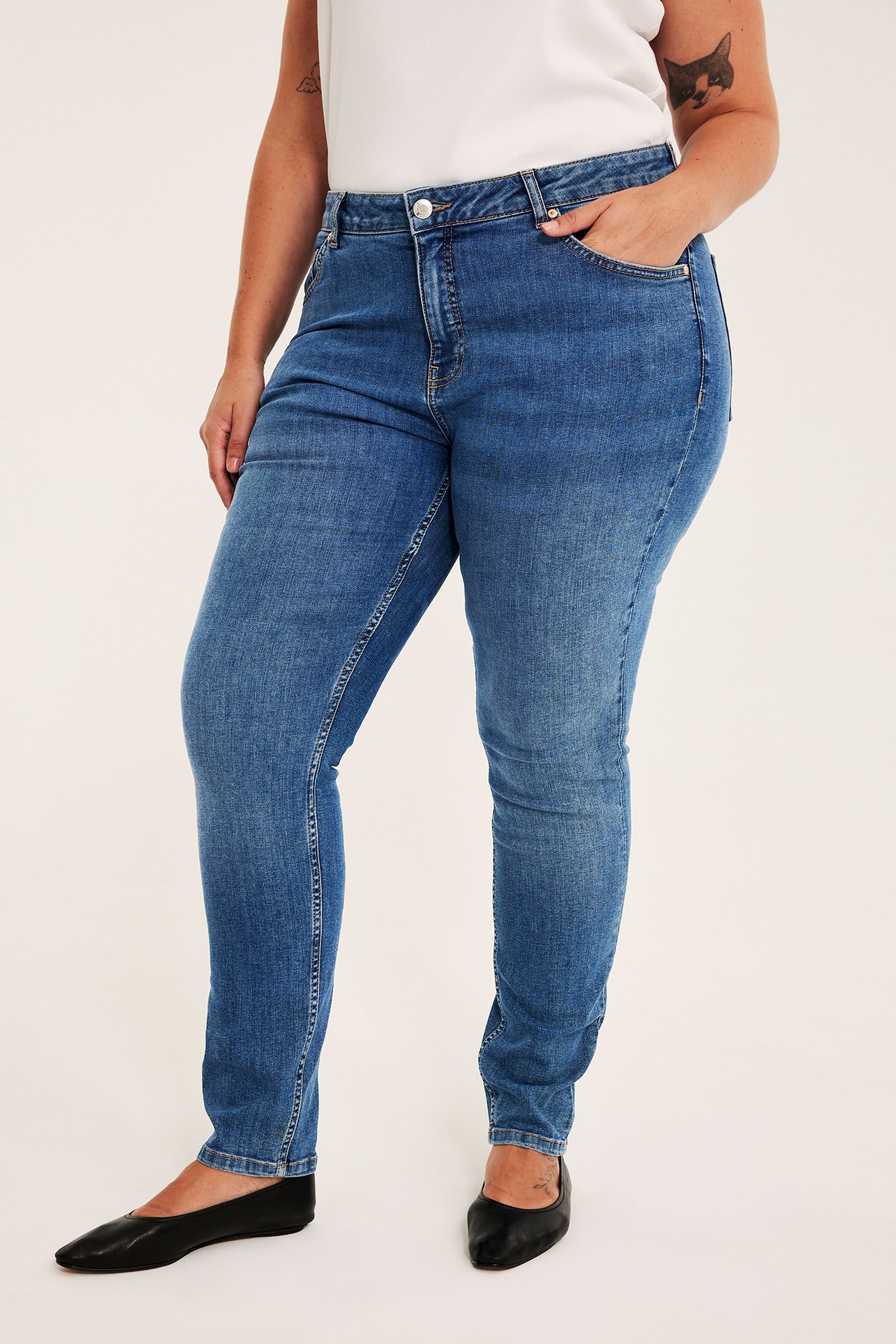 Frontbilde av kvinne i smale blå denimjeans, hvit topp og svarte flatsko.