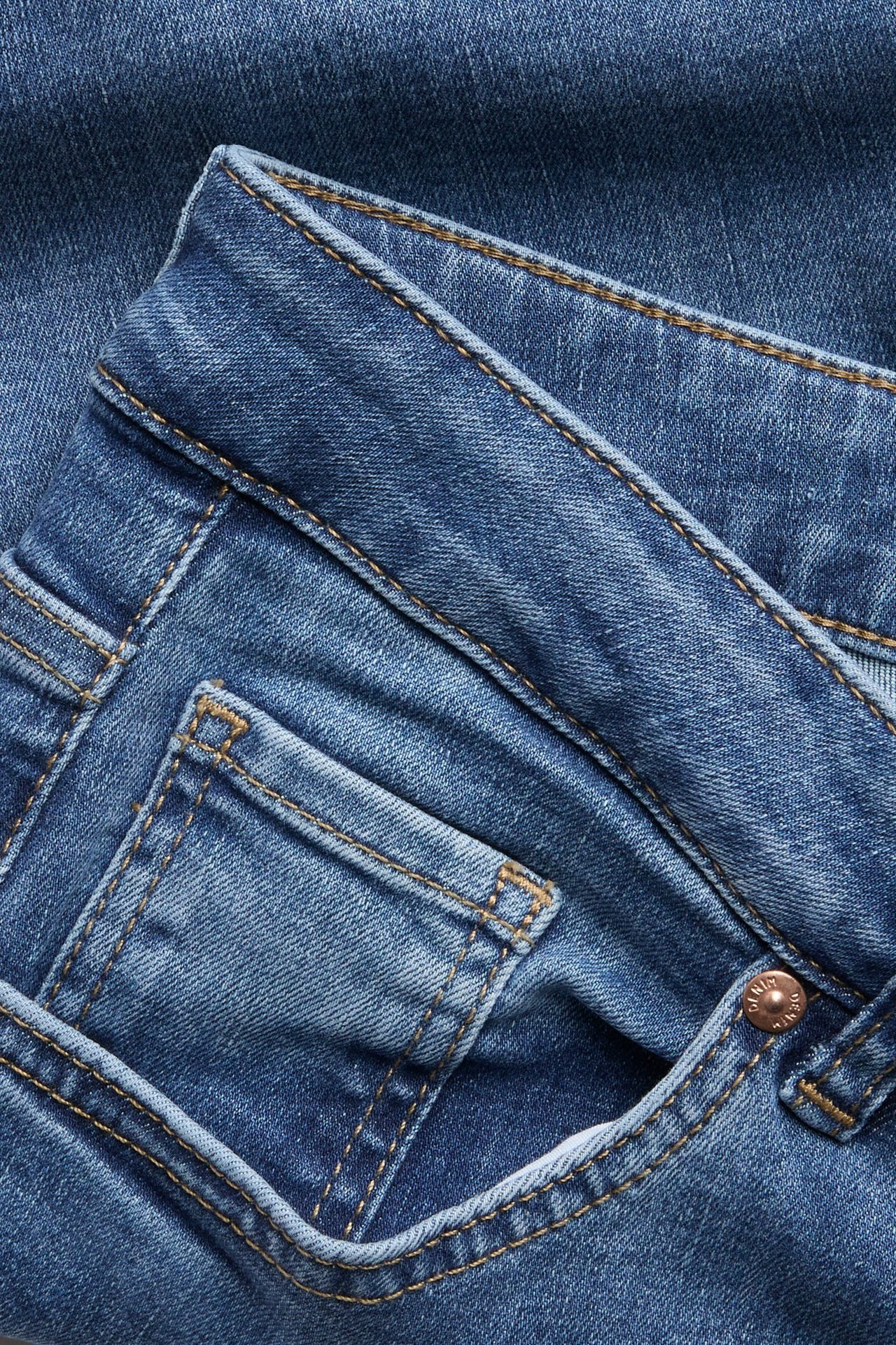 Lähikuva sinisistä denim slim high-waist farkuista kolikkotaskulla, vyölenkeillä ja metallinapilla.