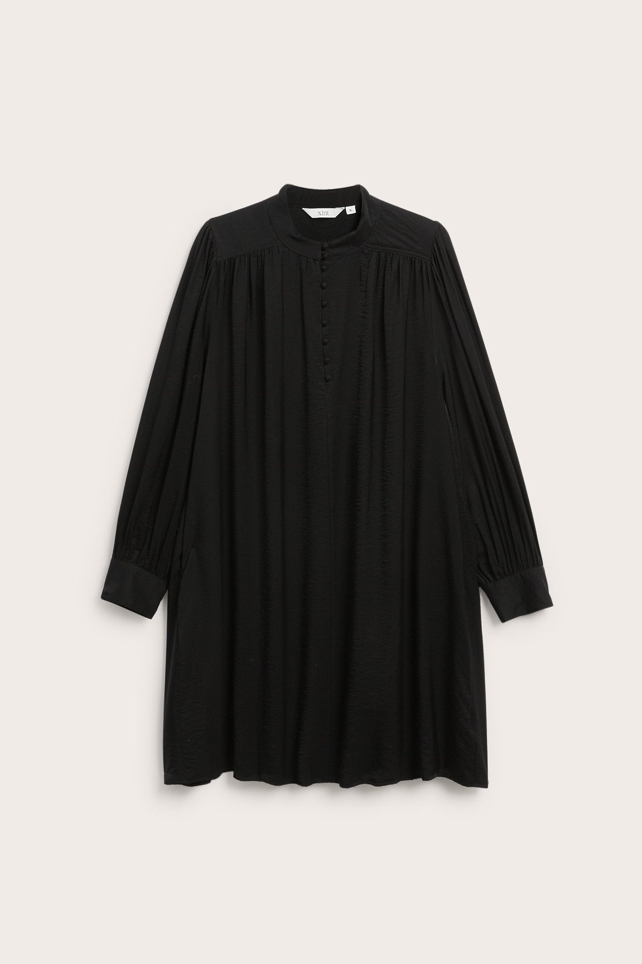 Front, svart langermet knelang kjole med knappestolpe og høy hals.
