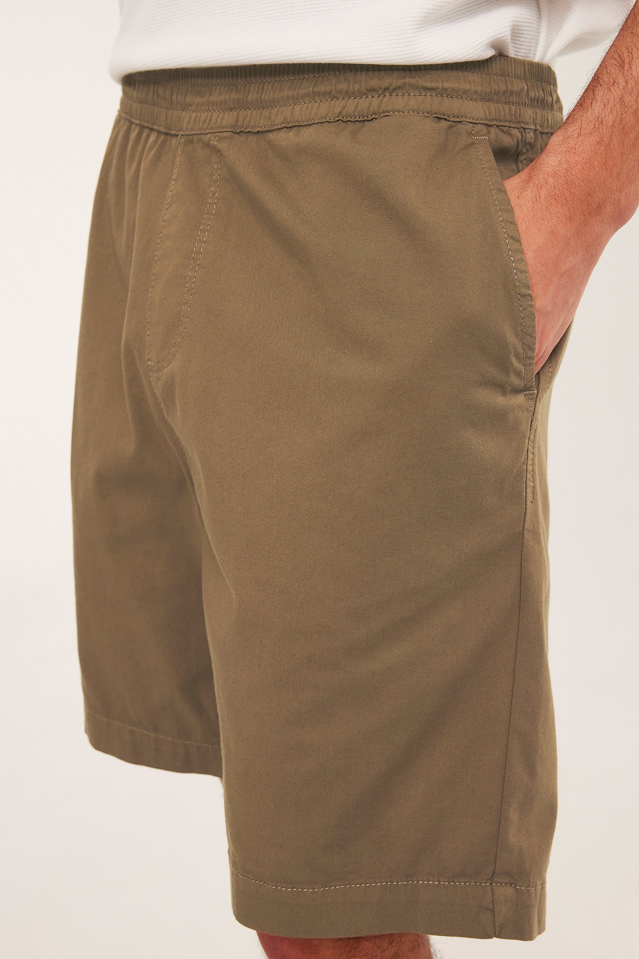 Miehen lähikuva sivulta, yllään ruskeat, väljät puuvillatwillishortsit ja valkoinen paita.