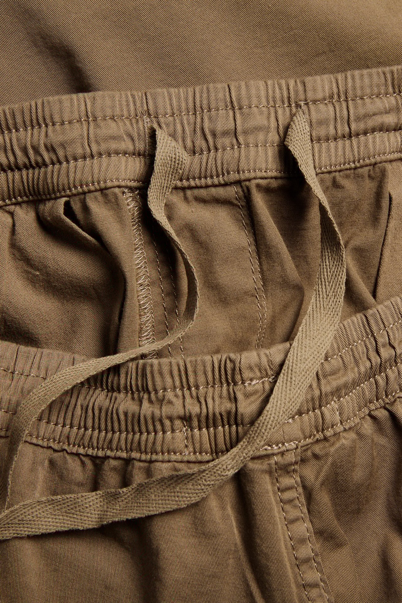Närbild av bruna shorts i bomullstwill med elastisk dragsko i midjan.