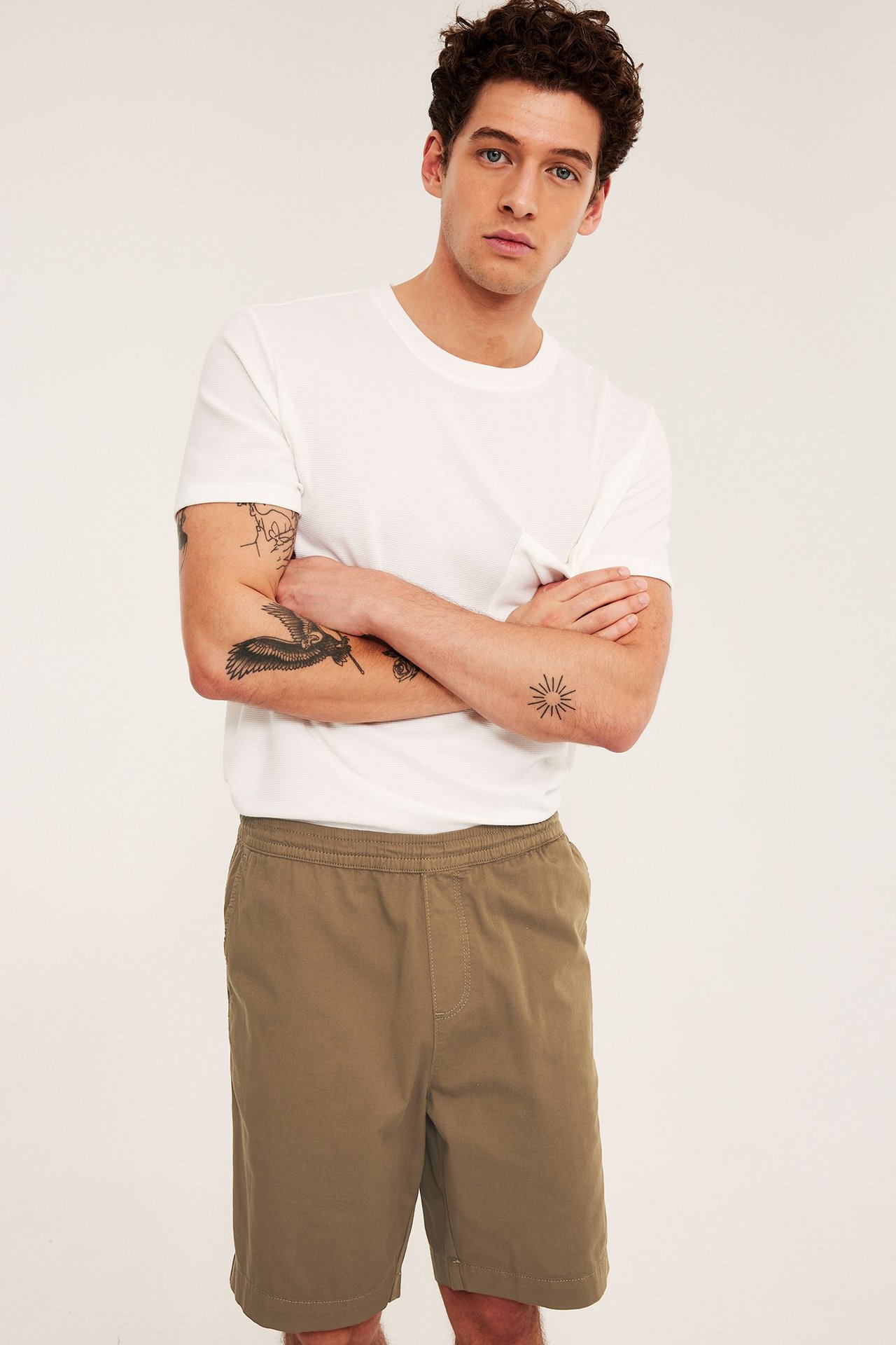 Frontvy av en man i löst sittande bruna bomullstwillshorts med resårlinning och en vit t-shirt.