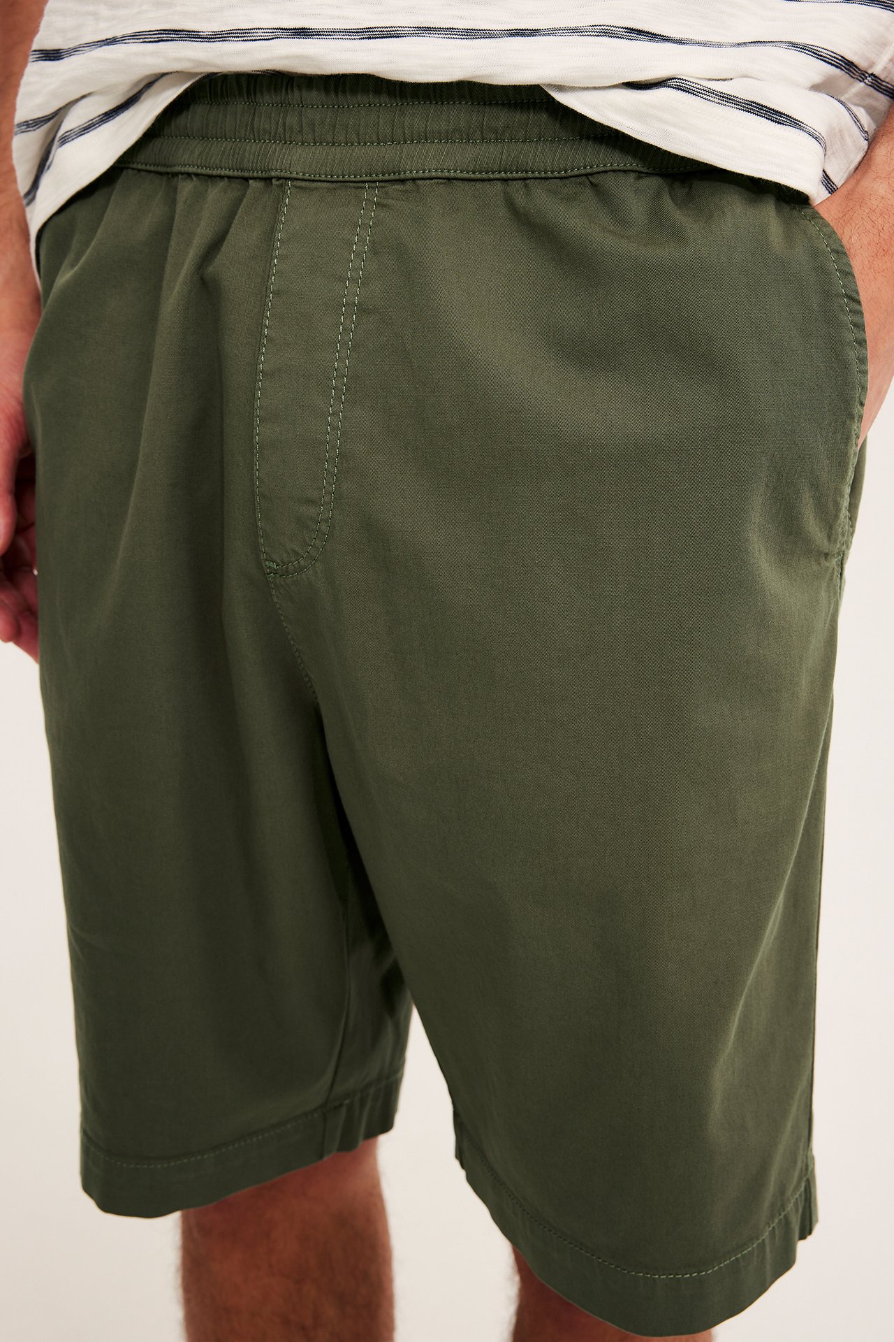 Lähikuva: mies yllään tummanvihreät väljät puuvillatwillishortsit, joissa joustava vyötärö, ja raidallinen t-paita.