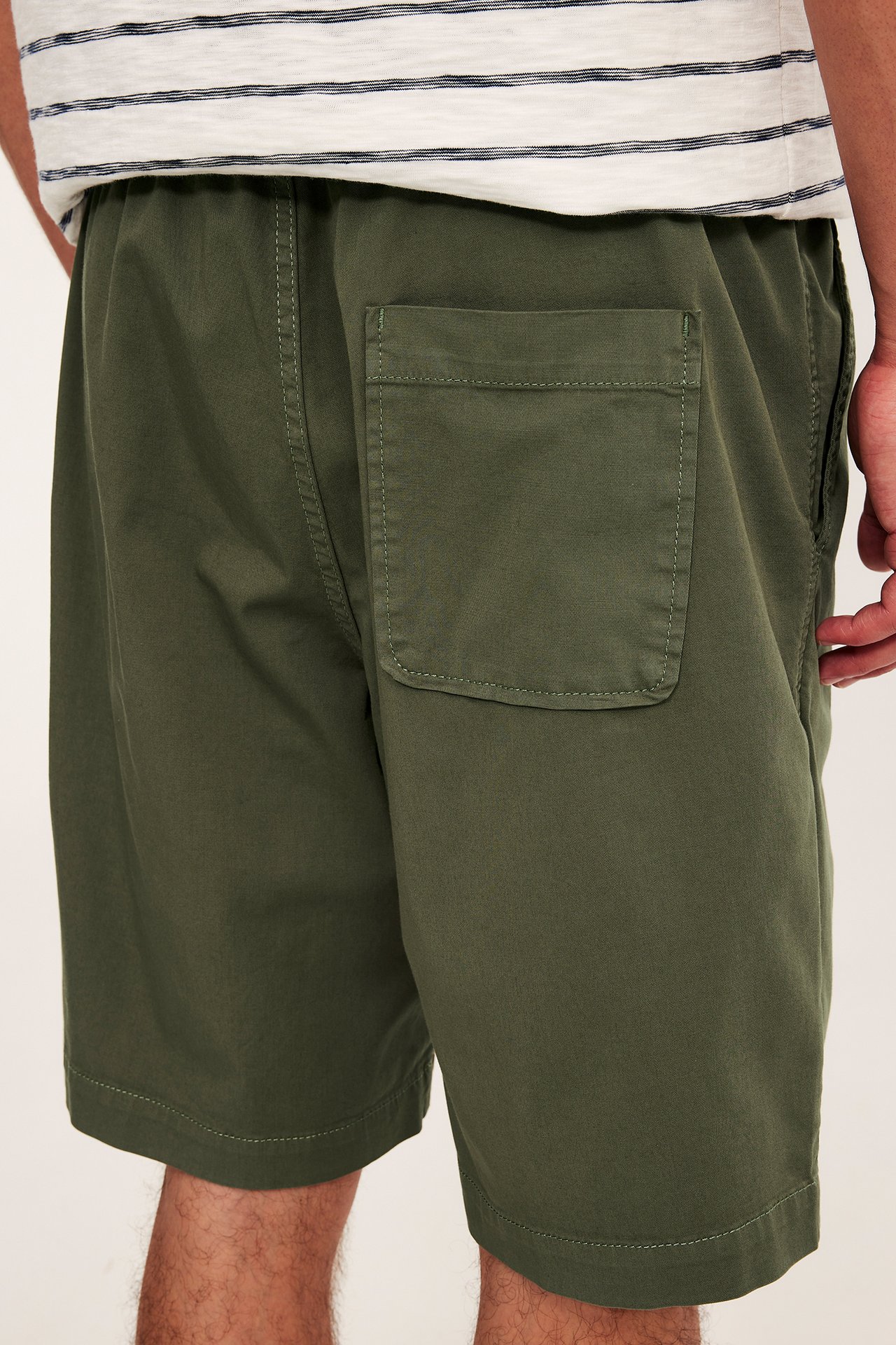 Mies takaa päin yllään väljät vihreät puuvillatwillishortsit takataskulla ja raidallinen t-paita.