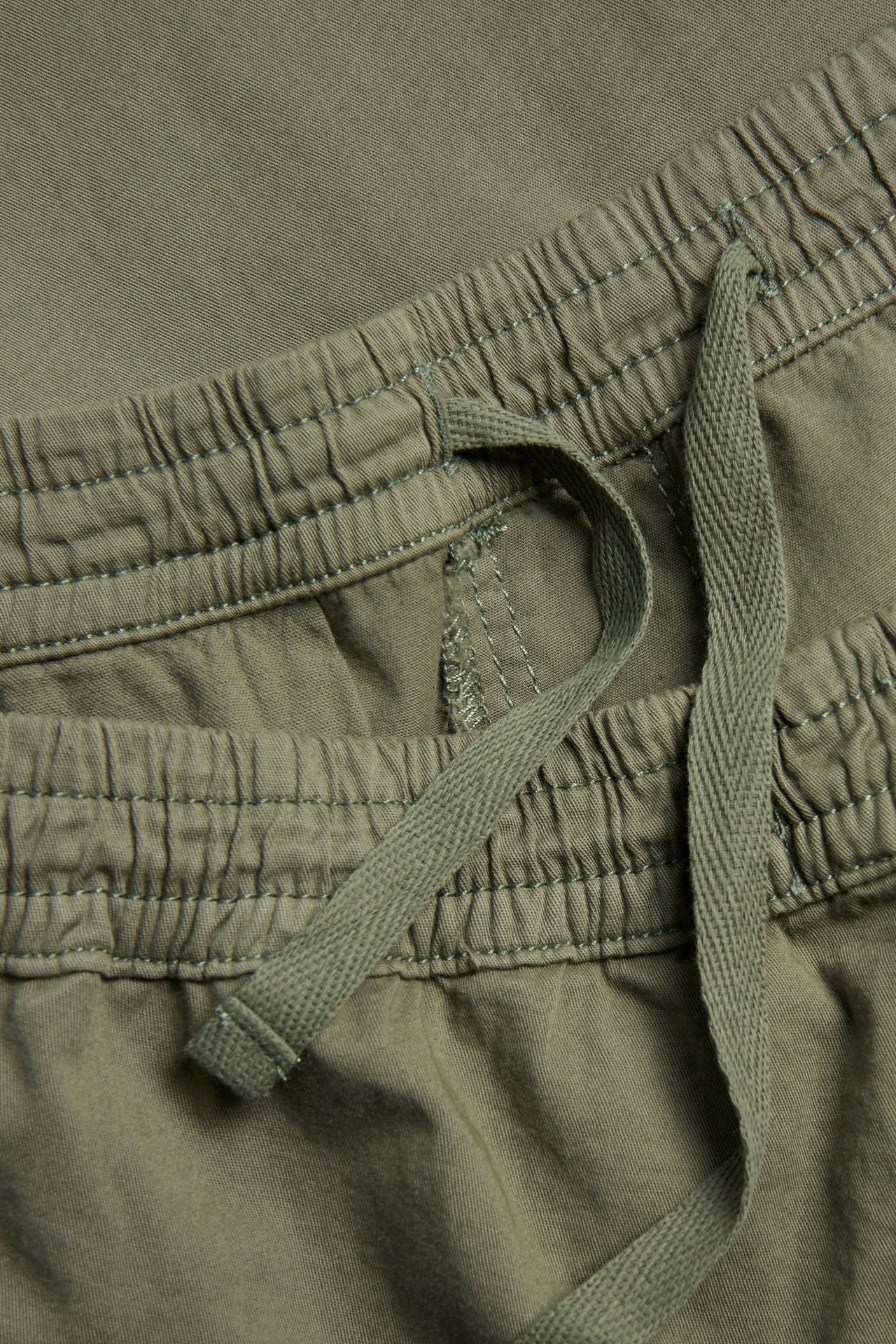 Närbild av gröna shorts i bomullstwill med elastisk midja och dragsko.