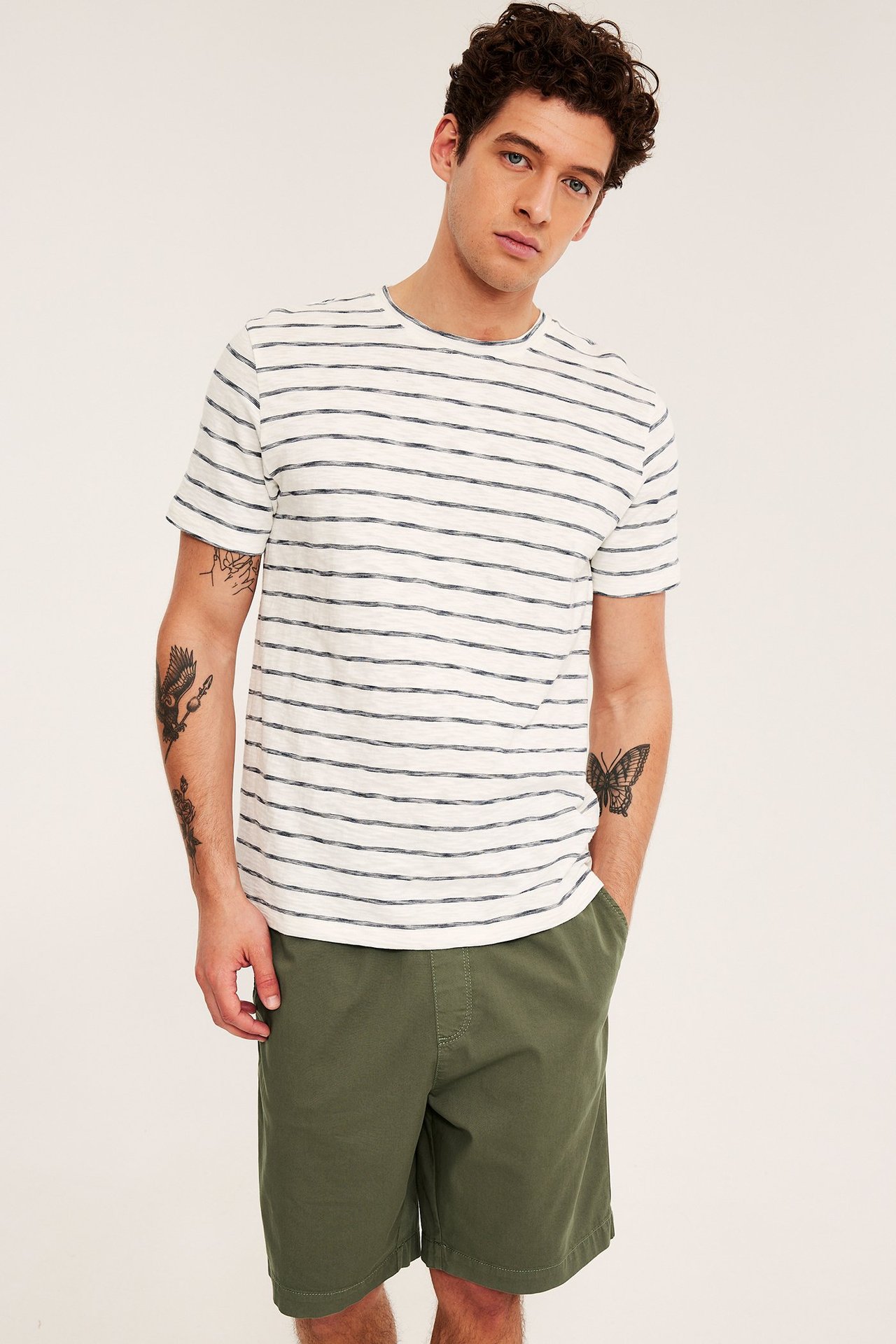 Framsida: Man i gröna lösa bomullstwillshorts med resårmidja och en randig t-shirt.