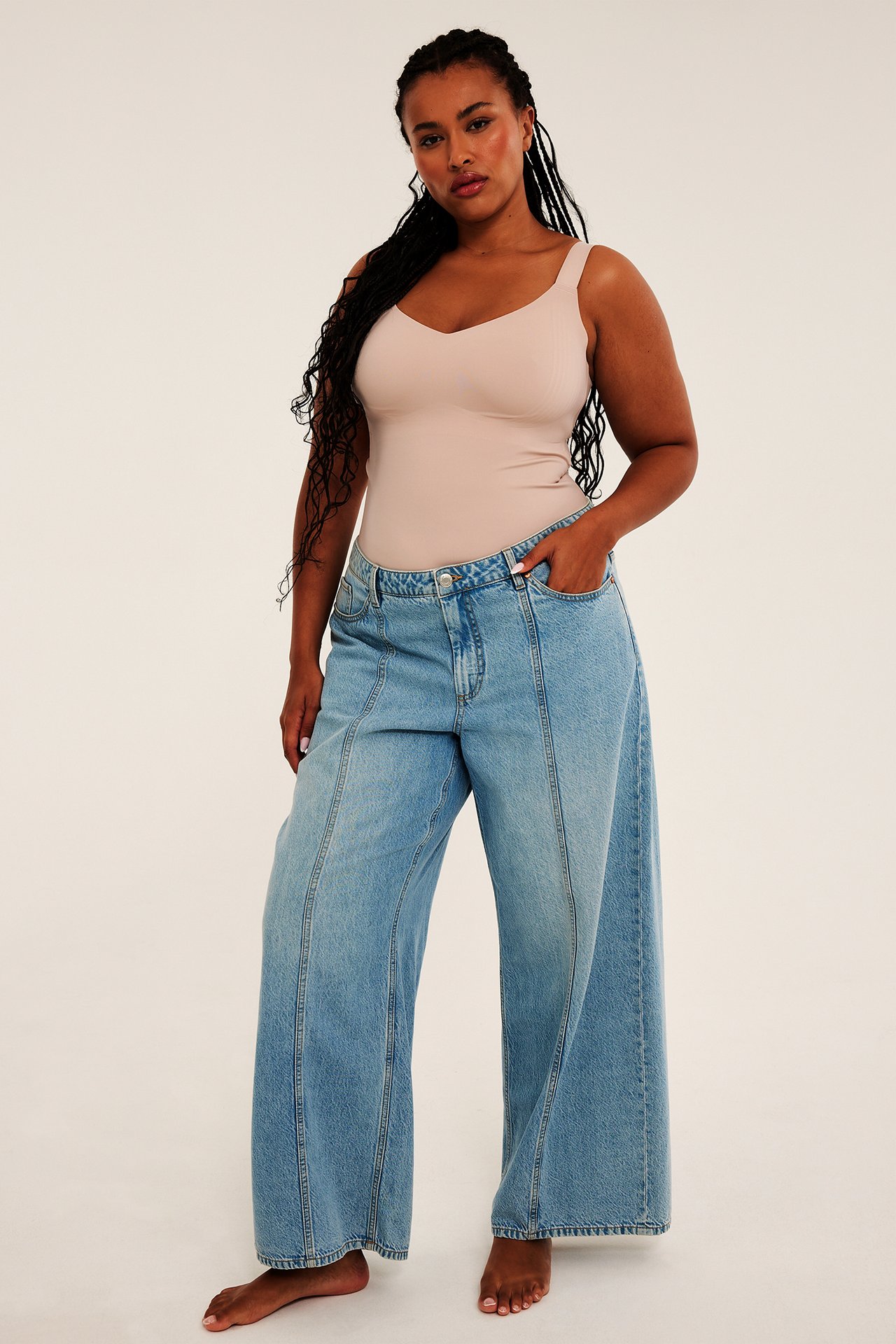 Frontvy av kvinna i ljusblå vida jeans och ett ribbat linne i beige.