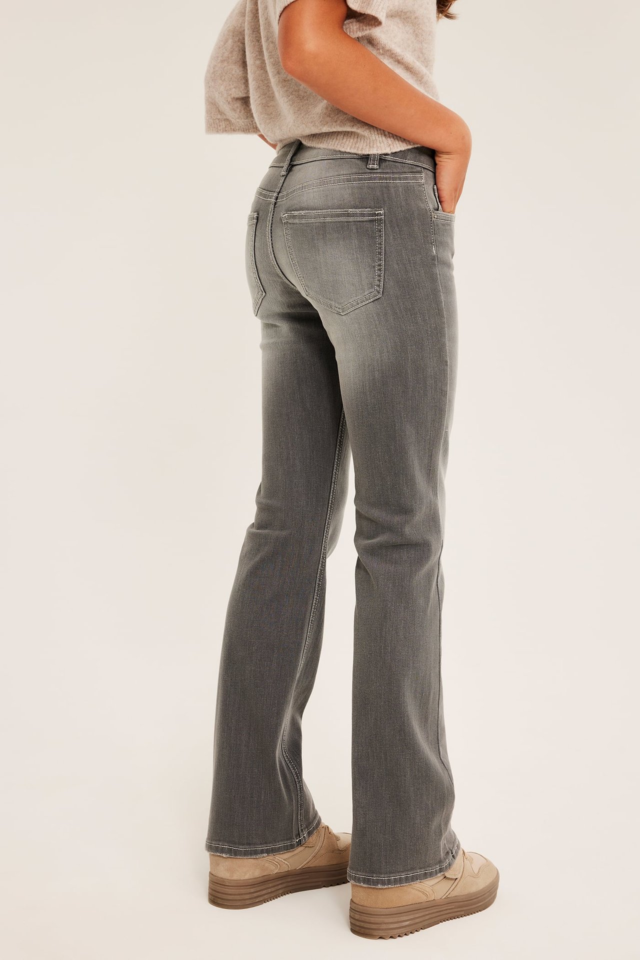 Sidovy av kvinna i grå utsvängda jeans, beige tröja och ljusbruna platåsneakers.