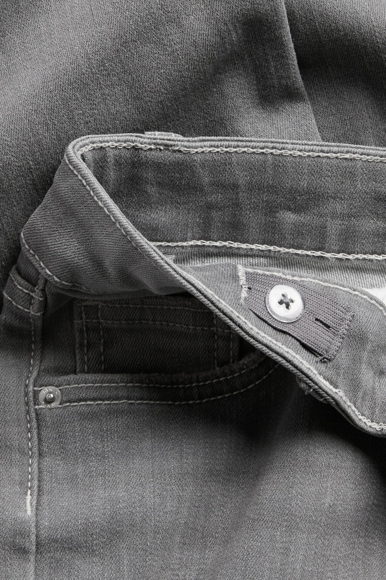Närbild på grå jeans med vit stjärnformad knapp, justerbar resårmidja och vita sömmar.