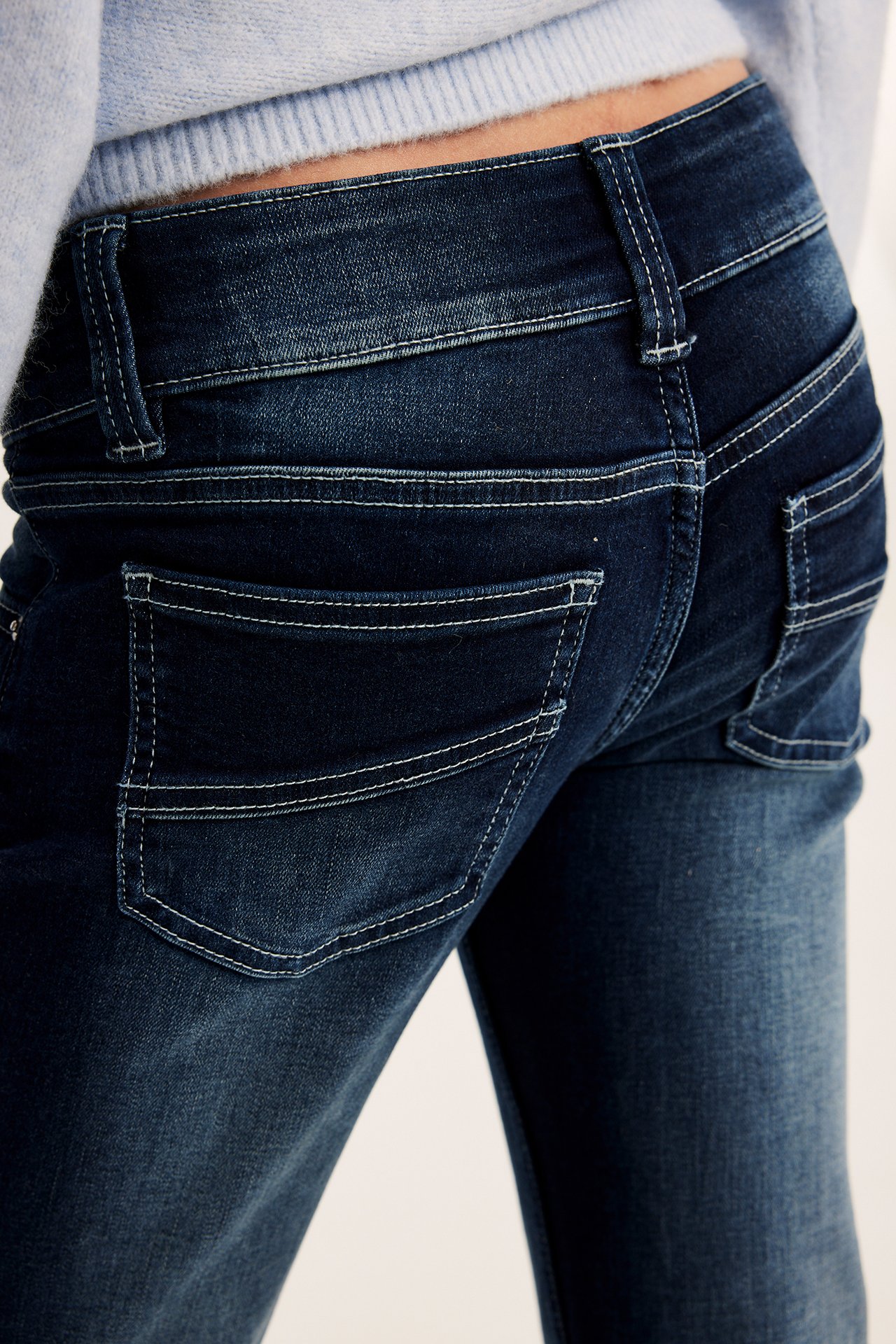 Bakifrån närbild: Mörkblå jeans med vita sömmar, fickor och ljusblå tröja.