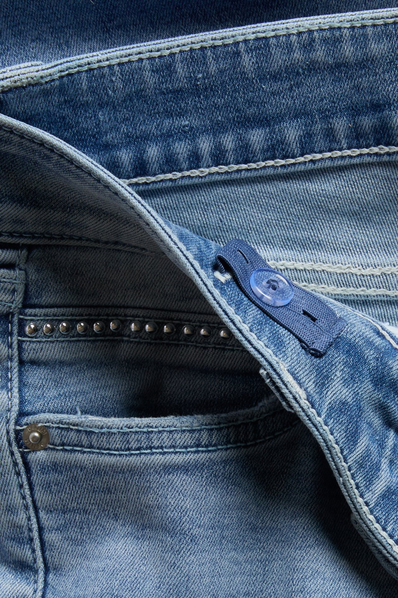 Närbild av ljusblå jeans med justerbar blå resår i midjan och nitar.