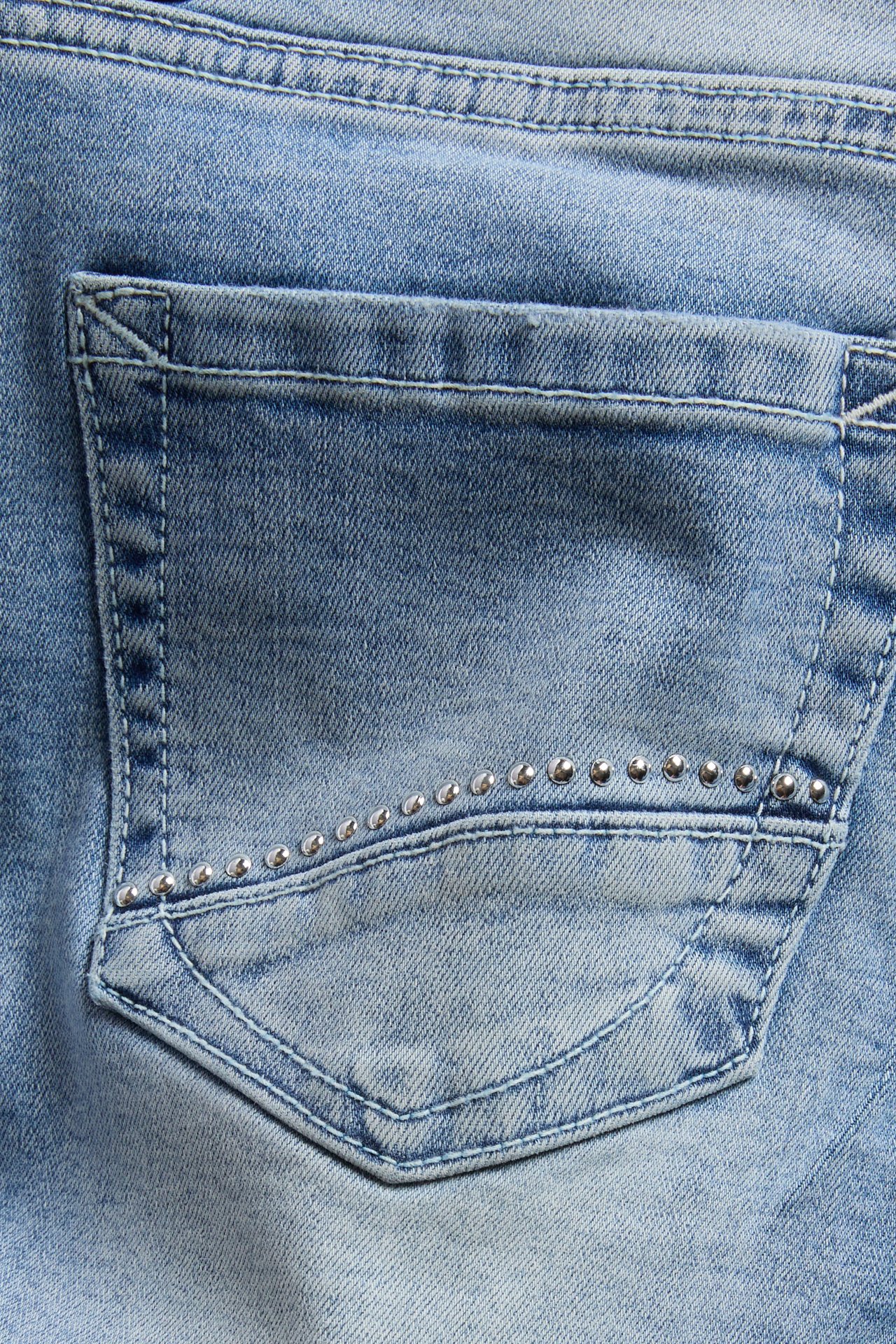 Närbild av ljusblå denimjeans bakficka med en rad silvernitar.