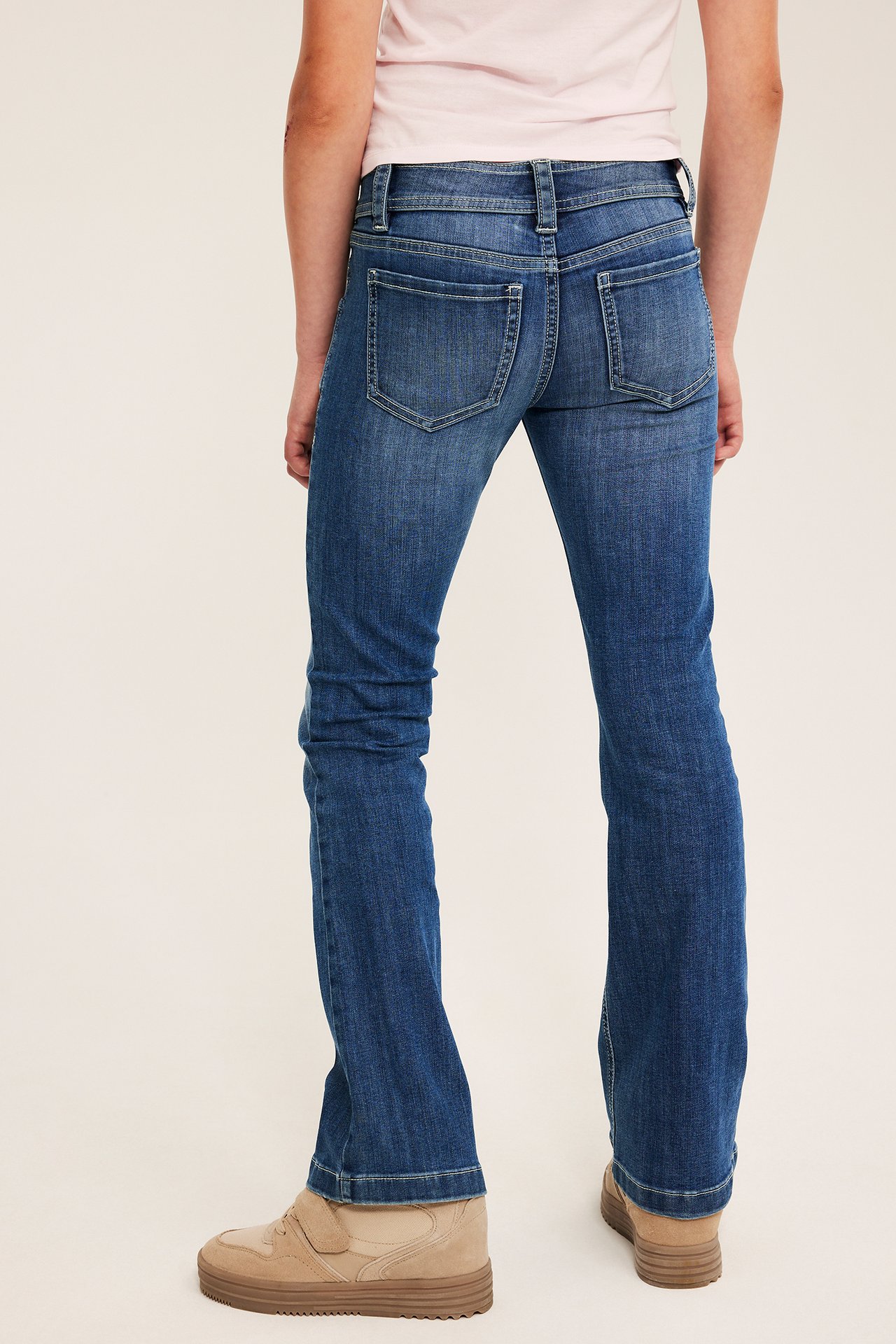 Bakfra av barn med blå utsvungne jeans og lysebrune ankelsko.