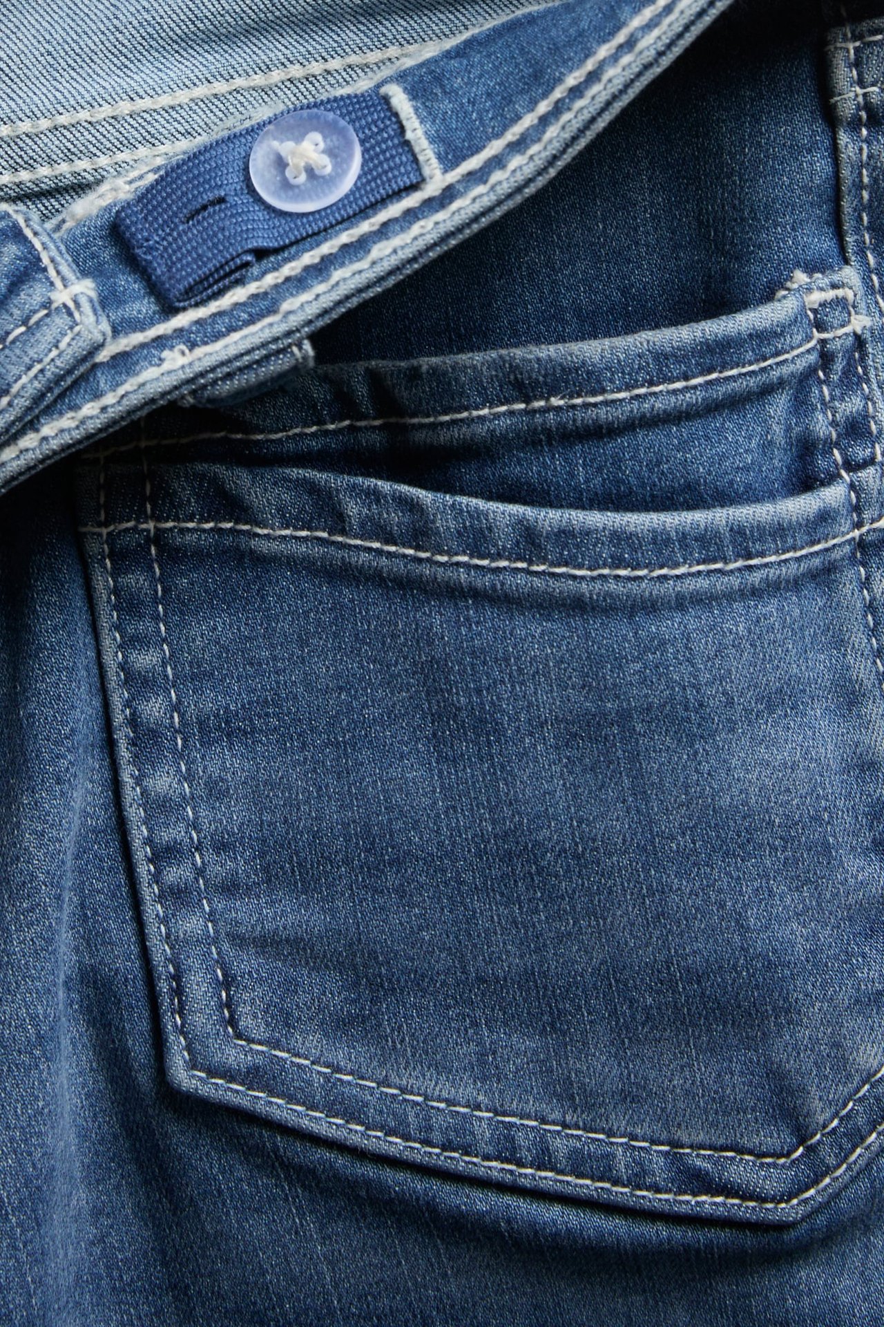 Zbliżenie na niebieskie jeansy bootcut dla dzieci, z przednią kieszenią i regulowaną elastyczną talią.