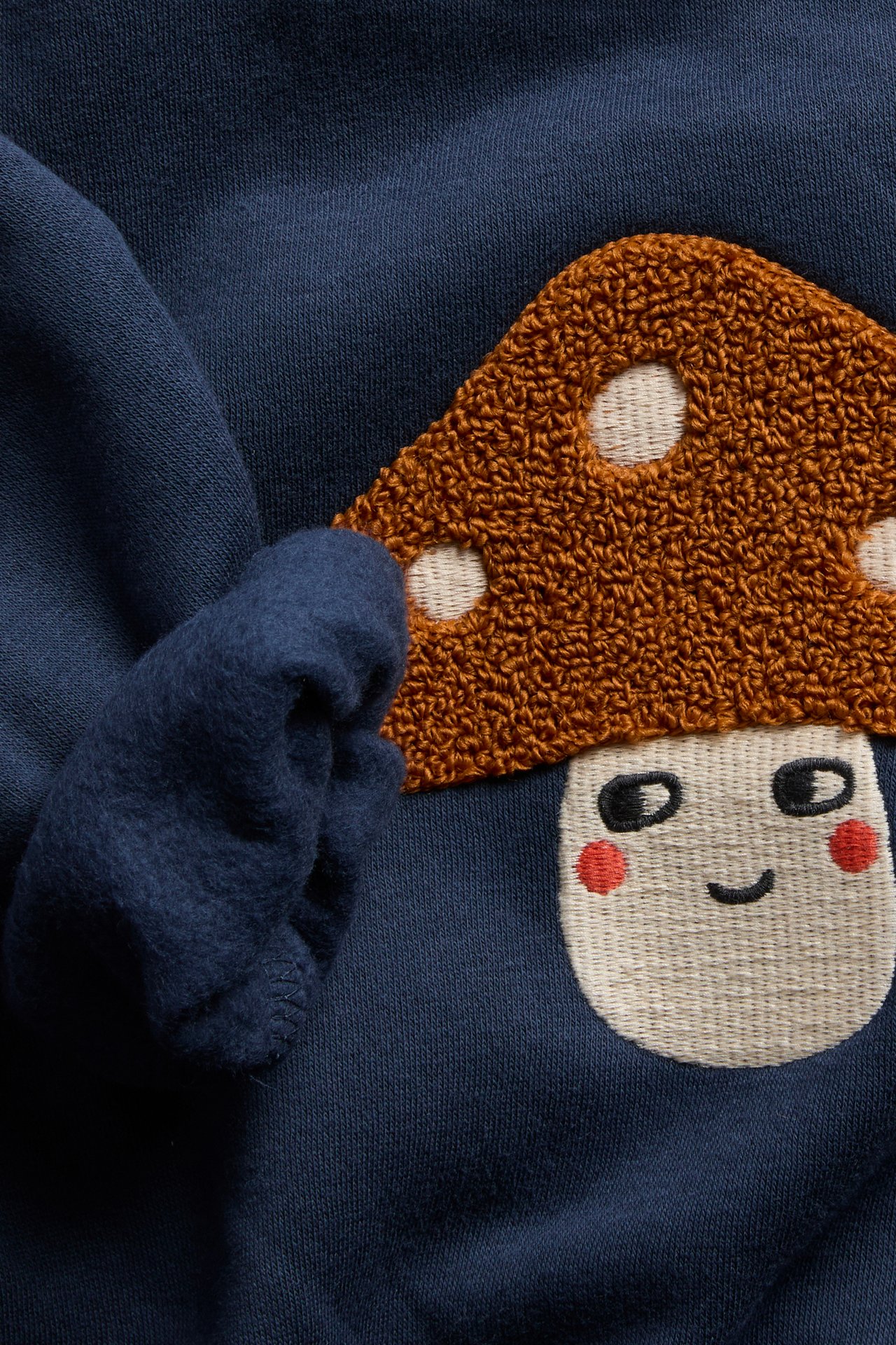 Närbild på en mörkblå tröja med broderad texturerad brun svamp med vitt ansikte.