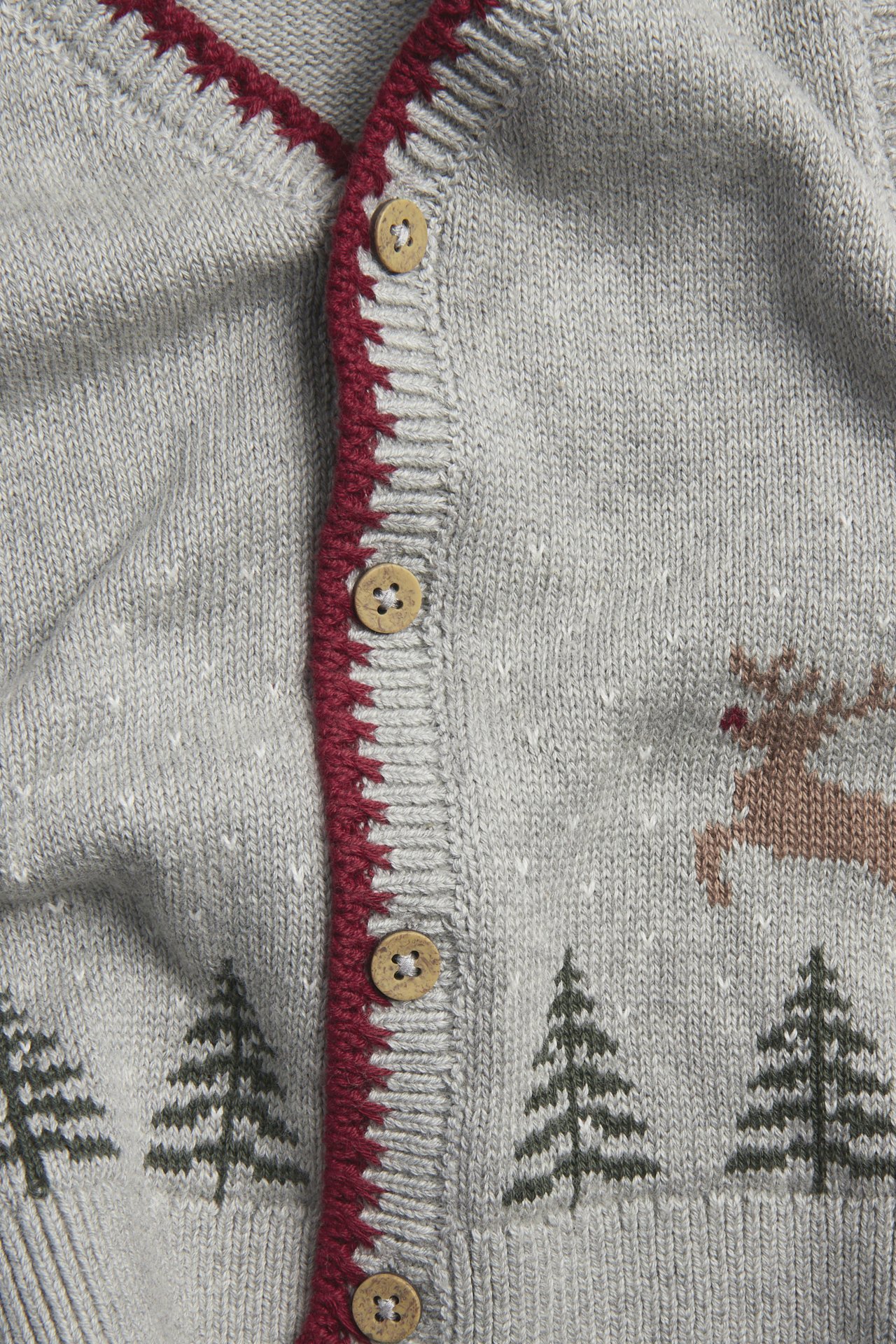 Zbliżenie szarego dzianinowego swetra z czerwoną lamówką, drewnianymi guzikami i zimowym wzorem.