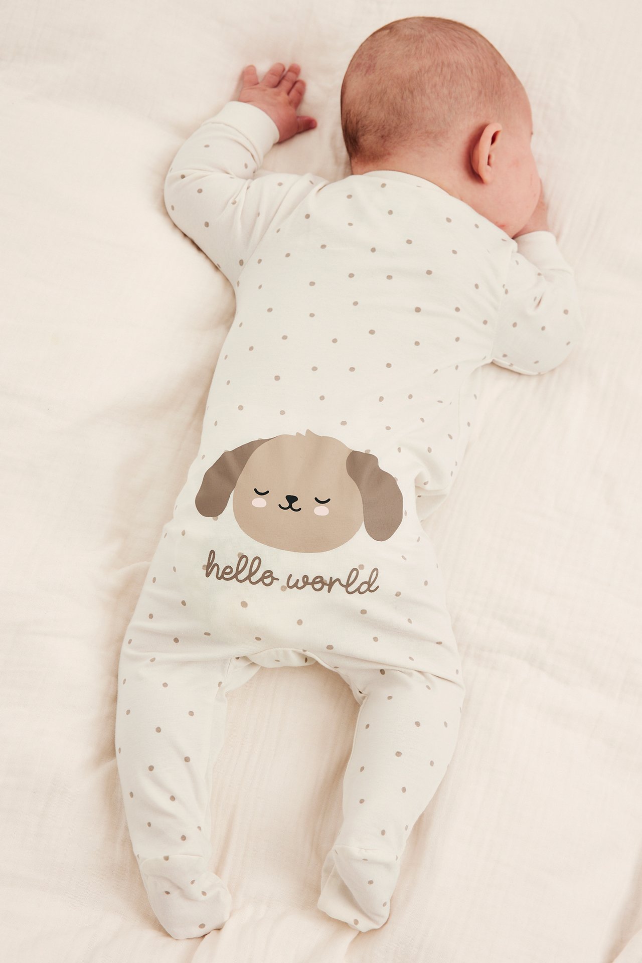 Widok z tyłu na dziecko w białym śpiochu w kropki z psem i napisem 'hello world'.