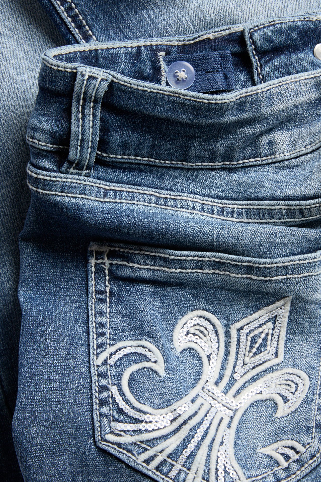 Zbliżenie na jeansy bootcut z niskim stanem, z białymi haftowanymi i cekinowymi kieszeniami, regulowana talia.