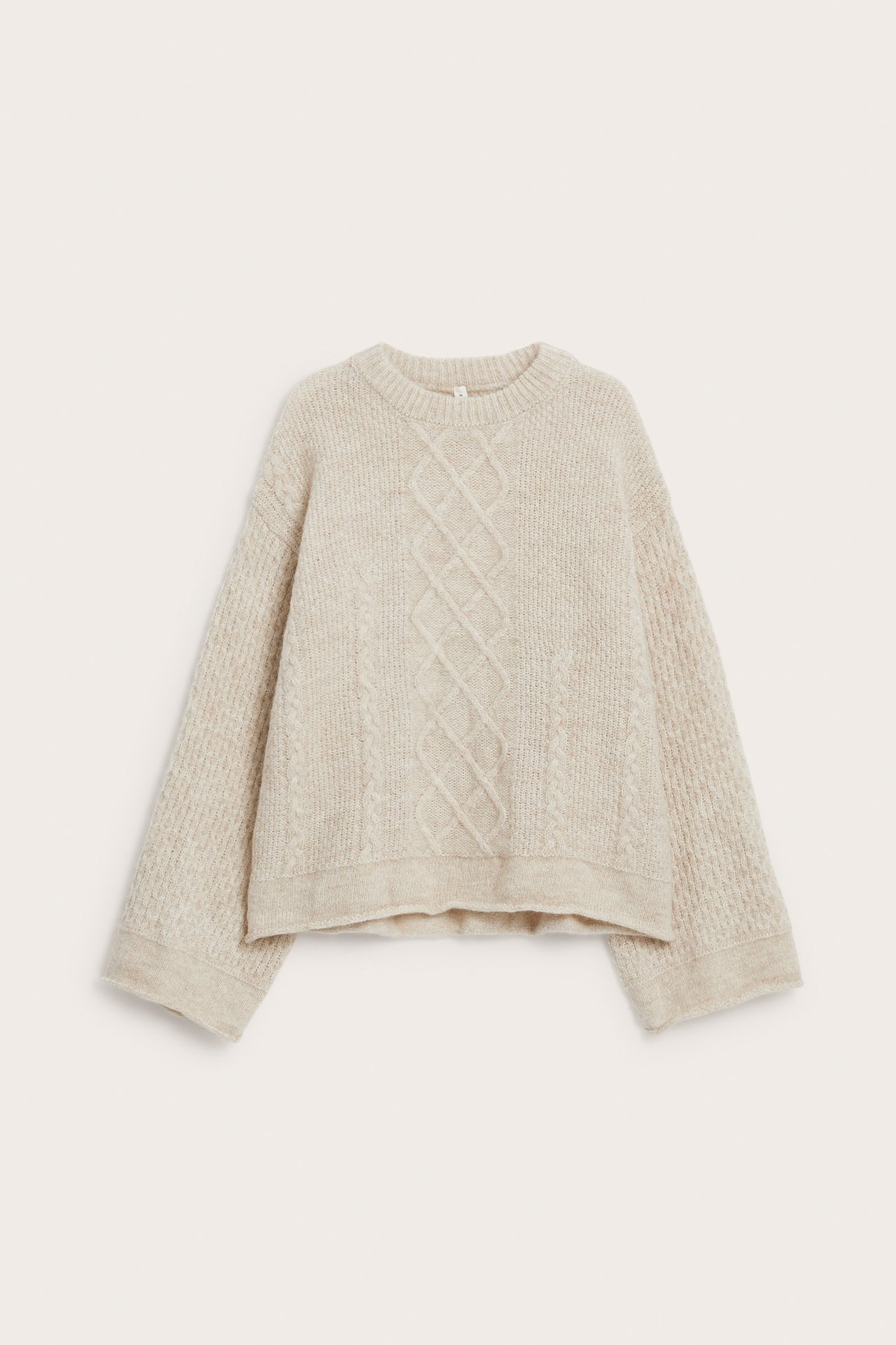Frontvisning av en lys beige løstsittende flettet strikkegenser.