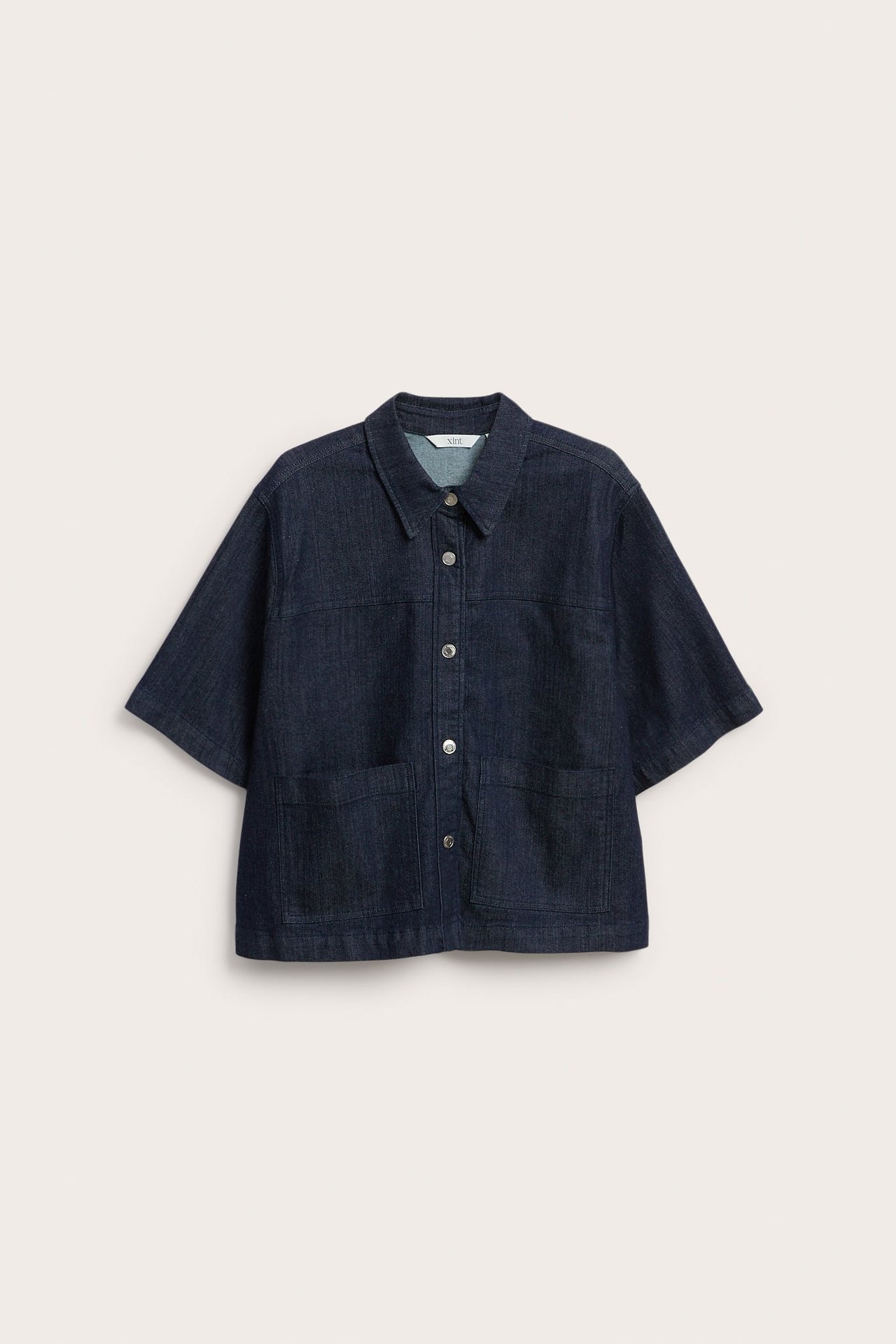 Frontvisning av mørkeblå denimskjorte med korte ermer, sølvknapper og to frontlommer.