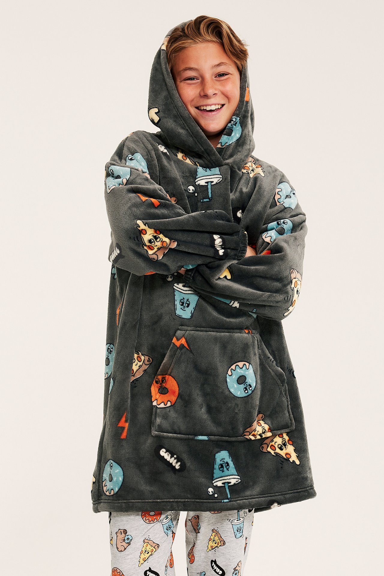 Forfra, smilende barn i en oversized mørkegrå lodden hettegenser med matmønster og grå mønstrete pyjamasbukser.