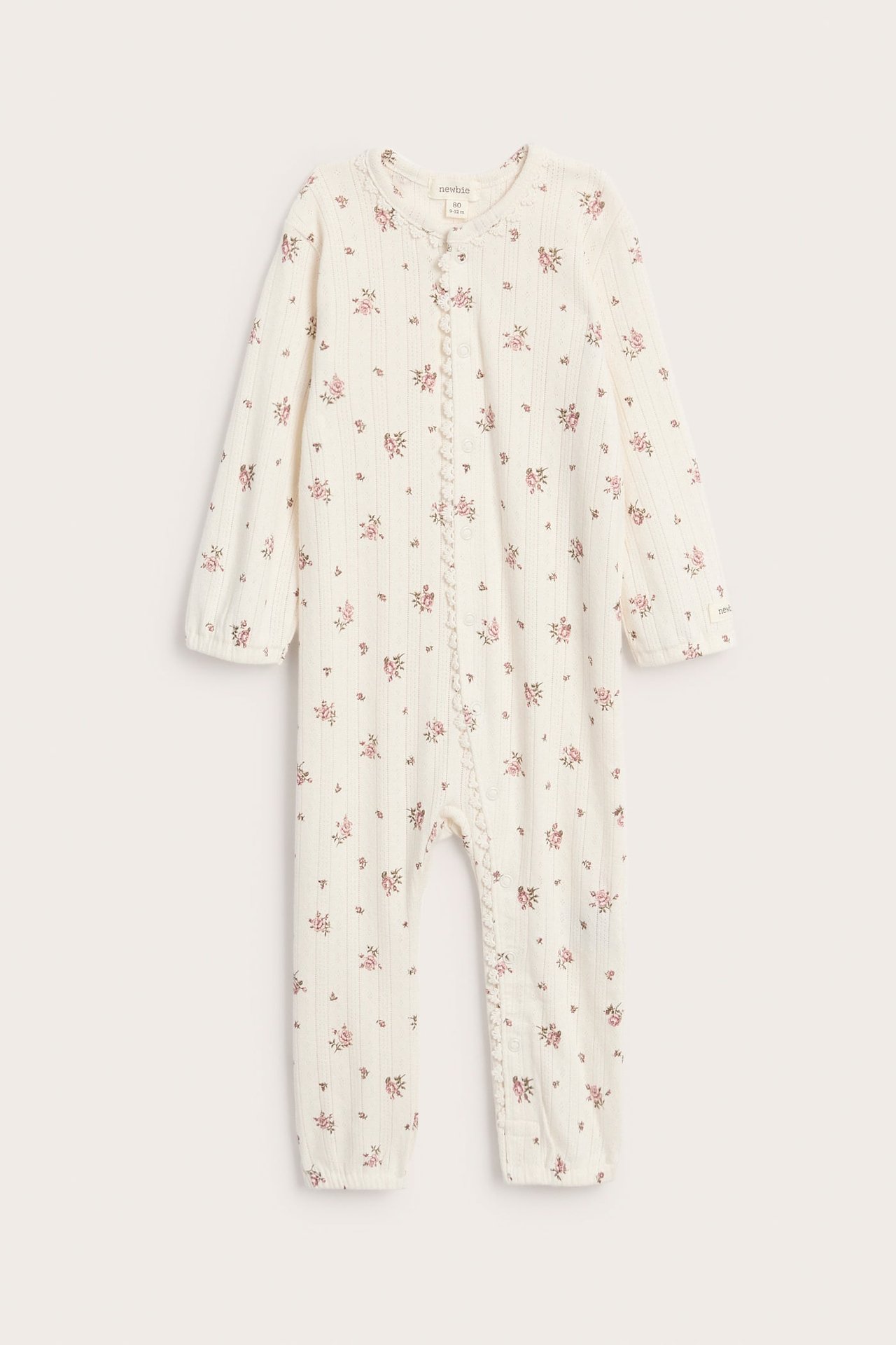 Frontvisning av en baby kremhvit ribbet sparkedress med rosa blomstermønster og trykknapper.