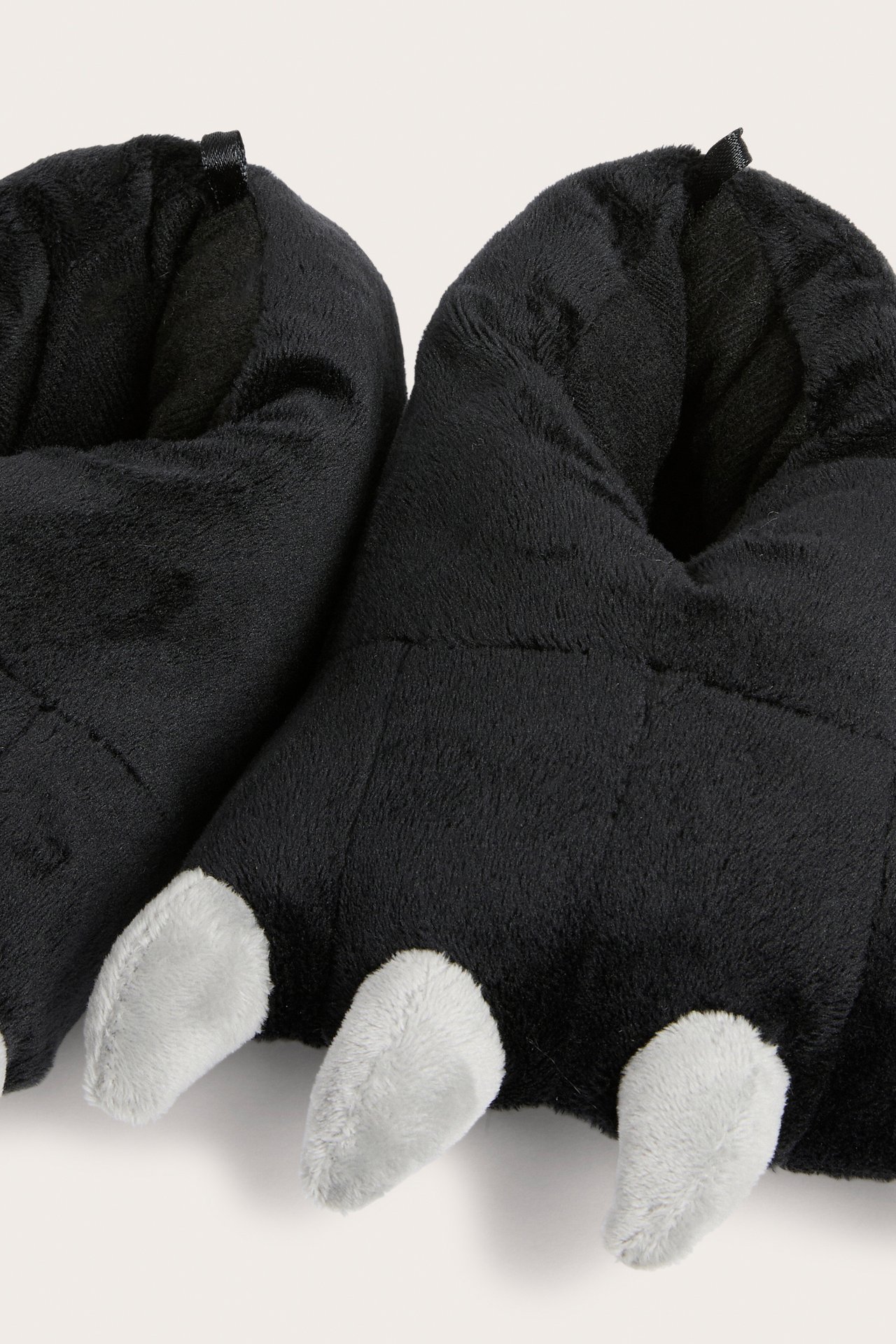 Närbild av två svarta plyschtofflor med vita klor.