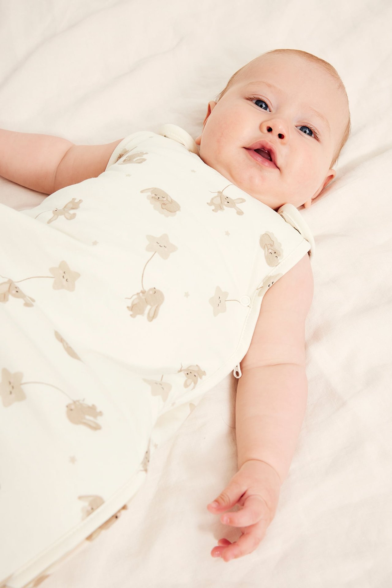 Frontbilde: baby iført lys beige sovepose med brunt kanin- og stjernemønster og glidelås i siden.