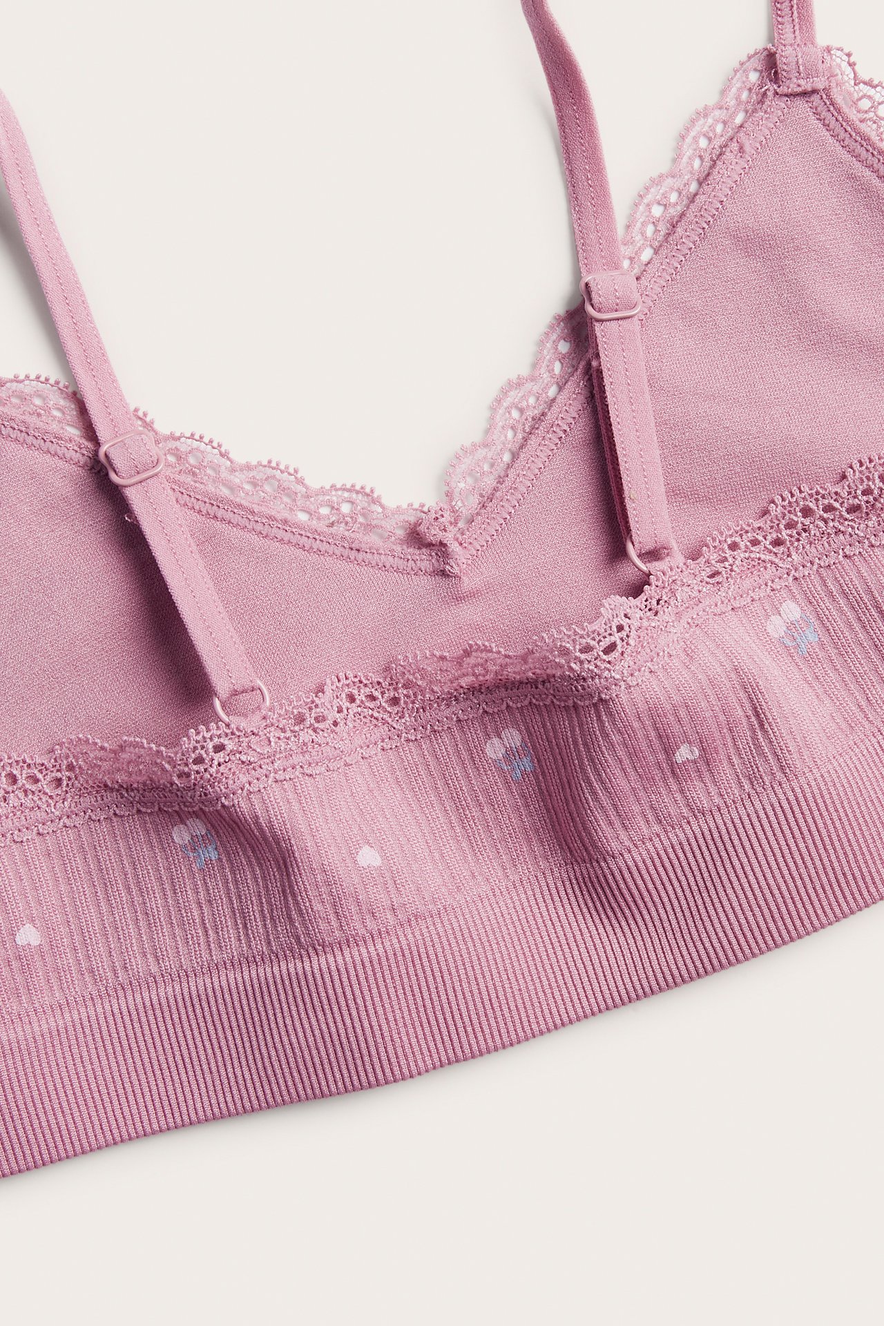 Närbild på en rosa ribbad bralette för dam med spetsdetaljer och små hjärtmönster.