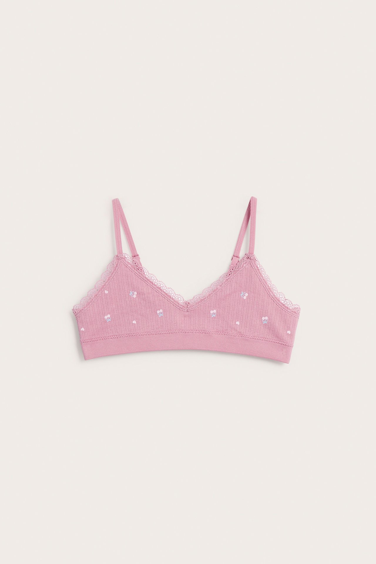 Framifrån, rosa ribbad bralette med vit spetskant och små blommiga detaljer.
