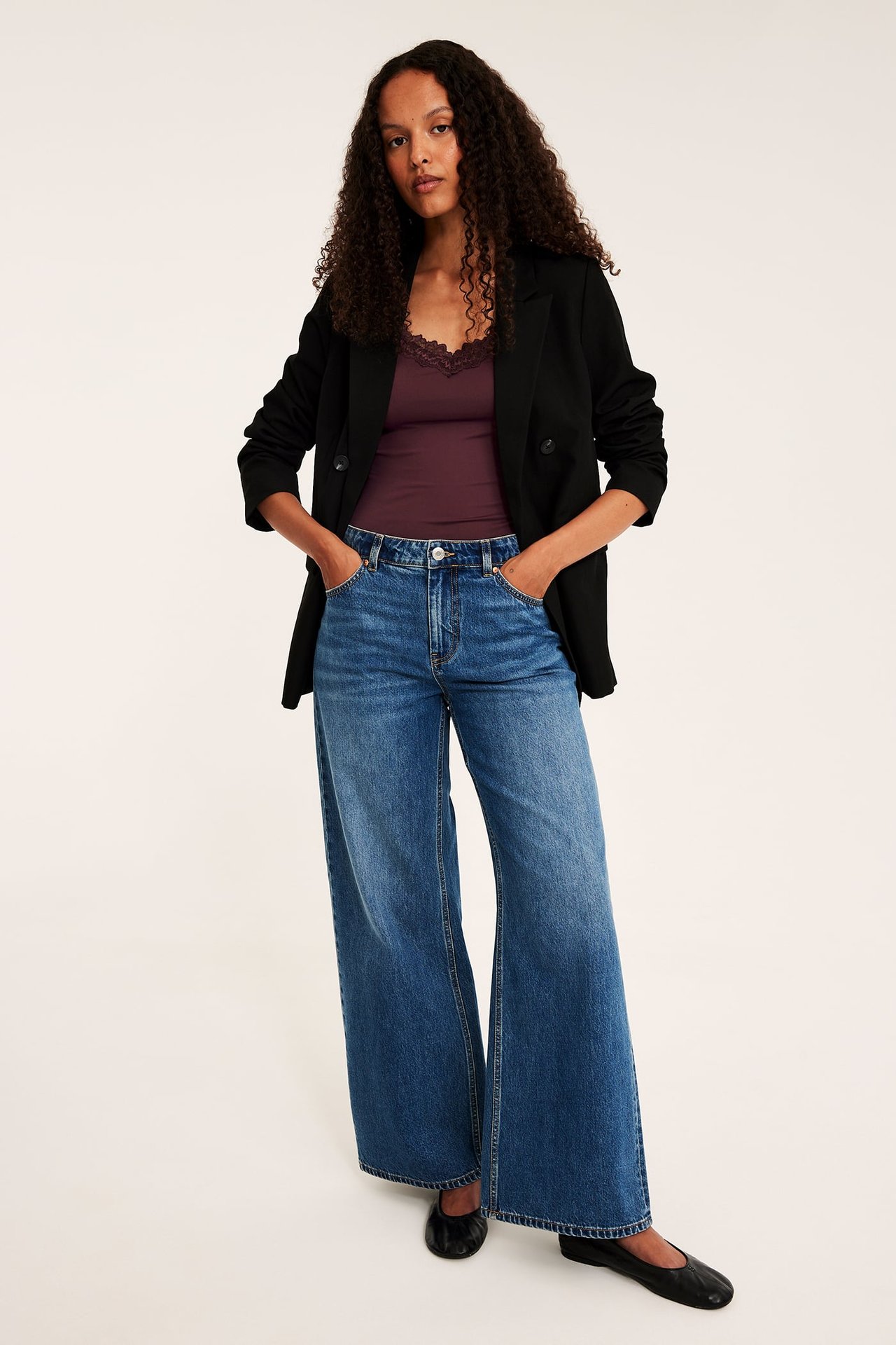 Kvinnelig modell i blå vide jeans, sort åpen blazer, lilla blondecamisole, sorte ballerinasko.