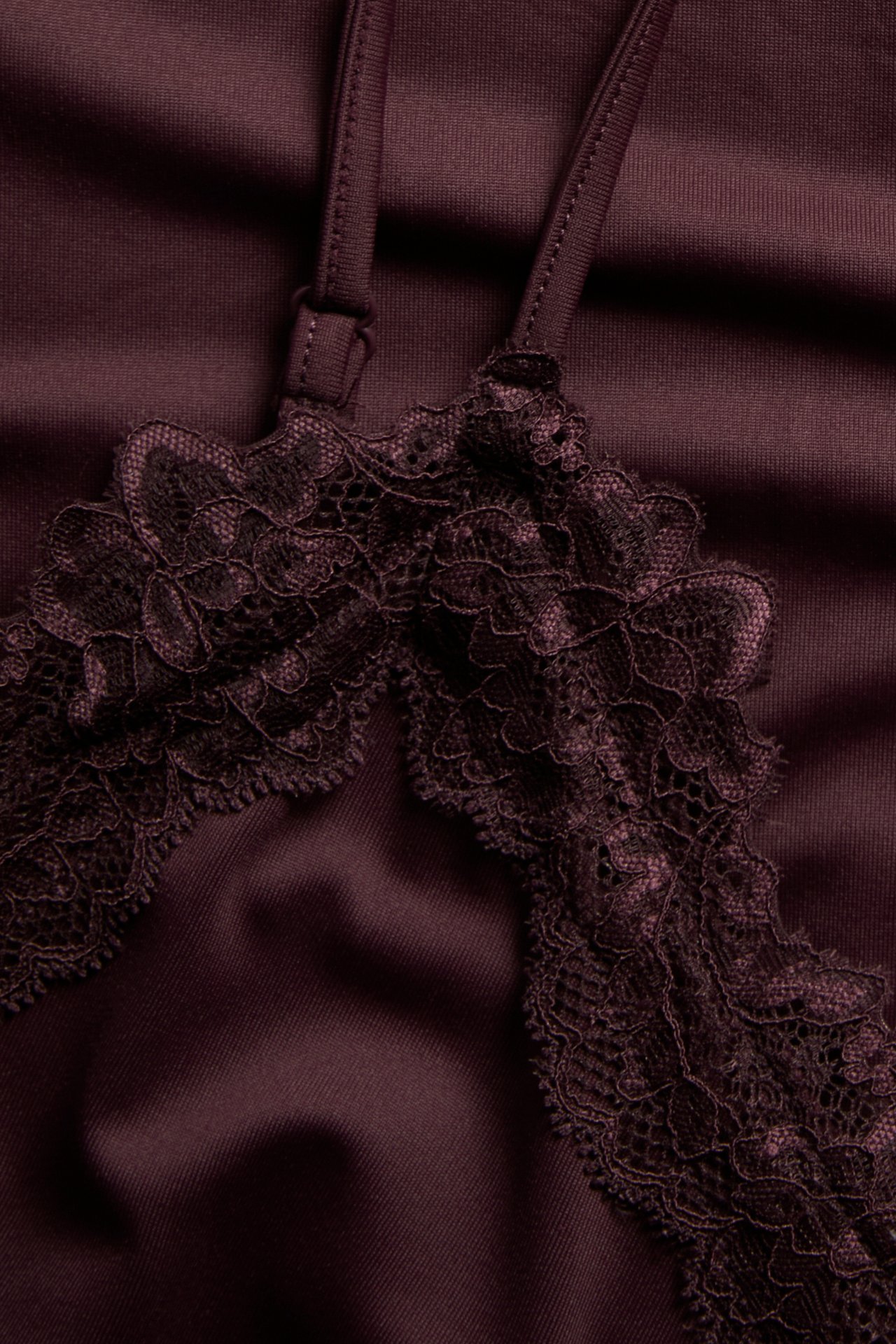 Närbild på en vinröd satin-camisole med blommig spetskant och justerbart axelband.