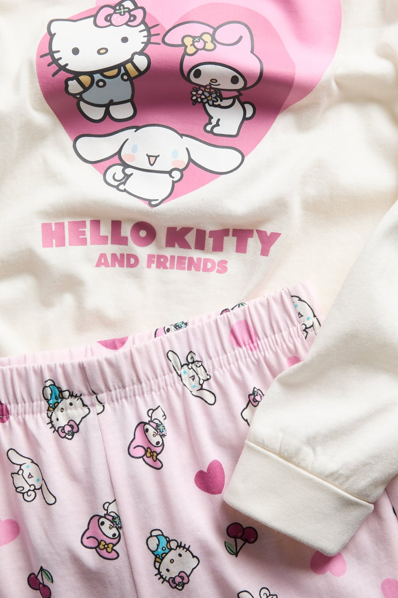 Nærbilde, forfra, av et barne Hello Kitty-pyjamassett med off-white topp og rosa mønstrede bukser.