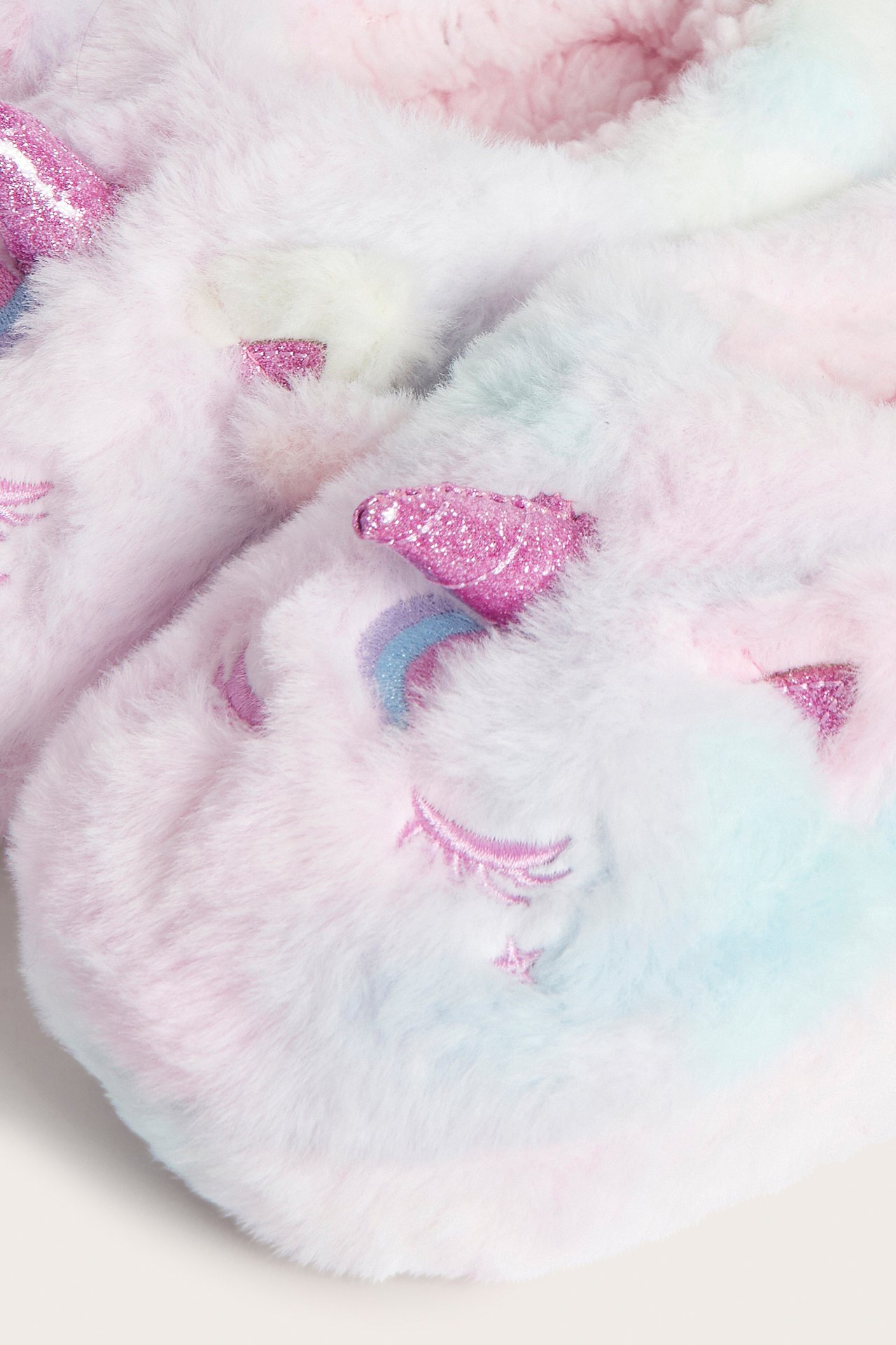 Närbild av pastellfärgade fluffiga enhörningstofflor med glitterhorn och broderade ögon.