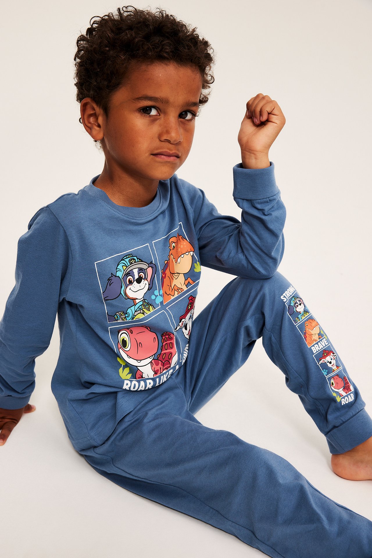 Front view, barn i blått bomullspyjamas-set med lång ärm och Paw Patrol- och dinosaurie-tryck.