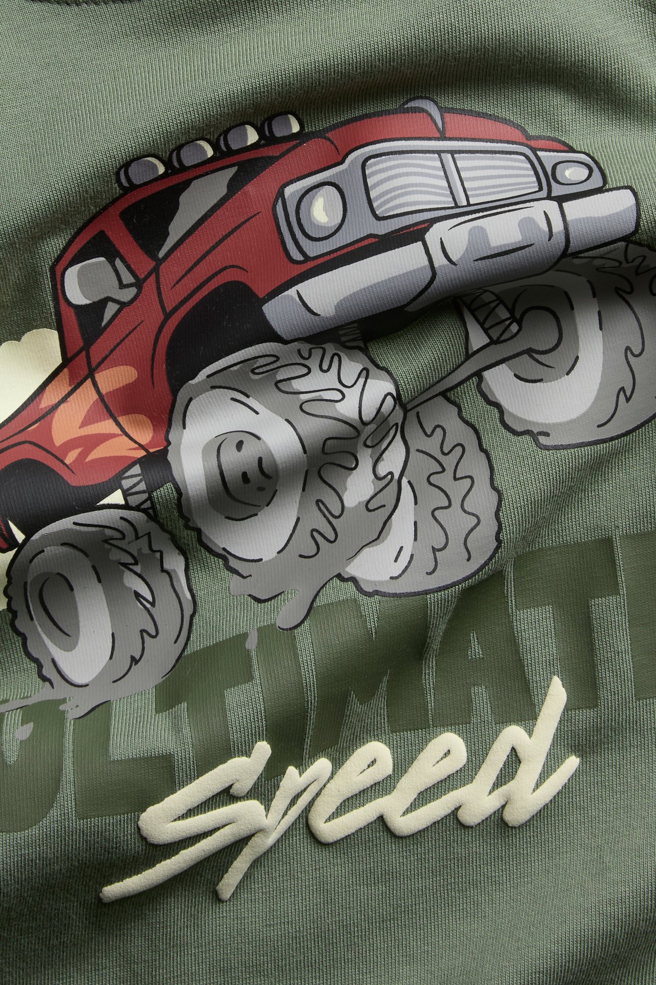 Zbliżenie przód: zielona bawełniana bluza dziecięca z czerwonym nadrukiem monster trucka i flokowanym napisem "Speed".