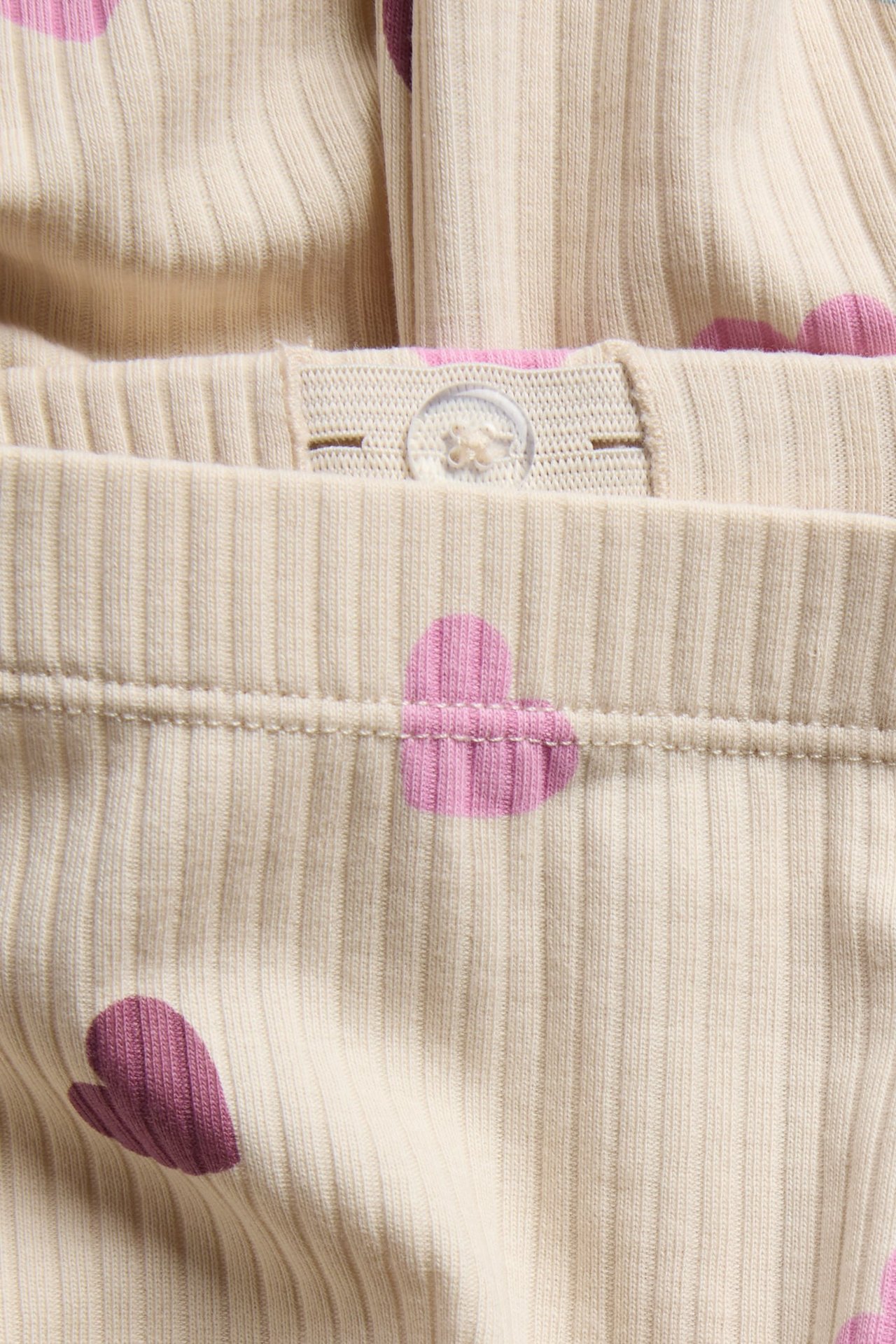 Närbild på beiga ribbade babybyxor med rosa hjärtan och justerbar midja med knapp.