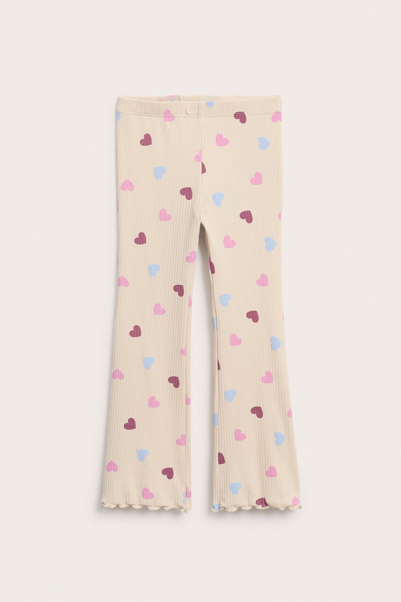 Framifrån: beiga ribbstickade utsvängda leggings för barn med färgglatt hjärtmönster och vågig kant.