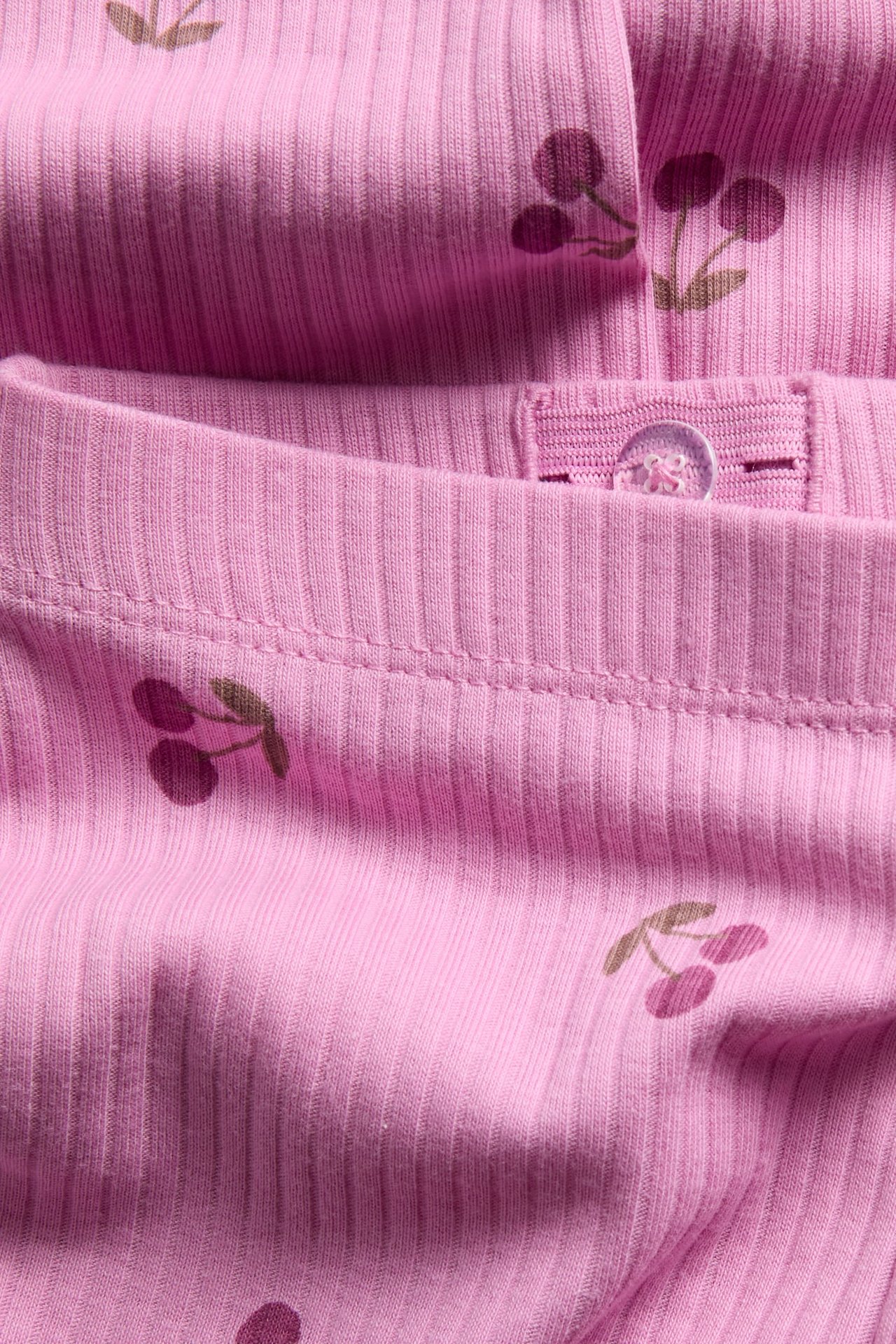 Närbild av rosa ribbad trikåplagg med körsbärstryck och justerbar knappmidja.