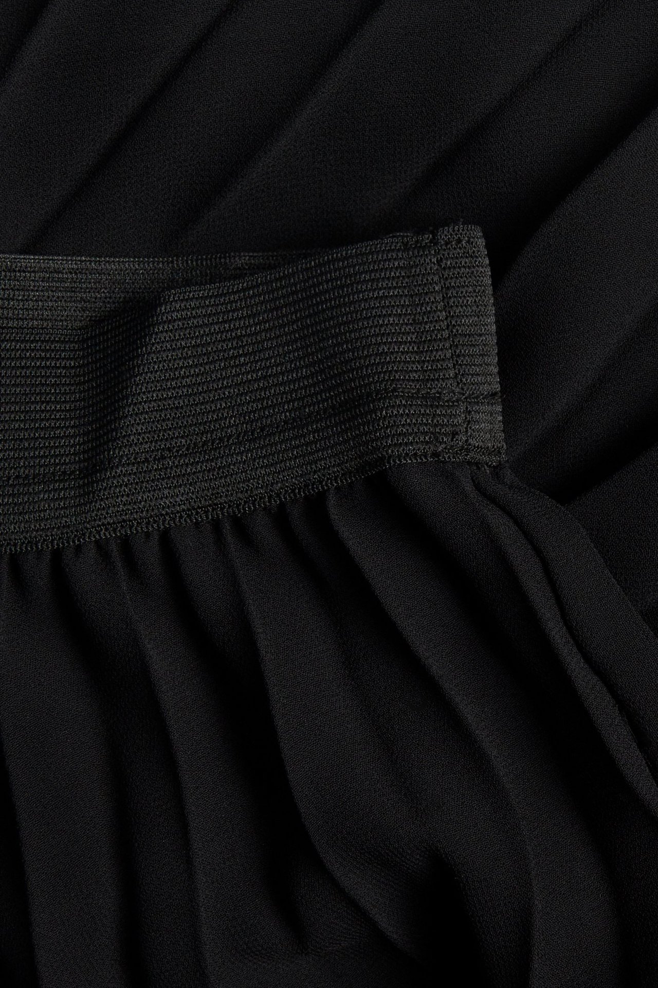 Närbild av en svart plisserad långkjol med elastisk midja.