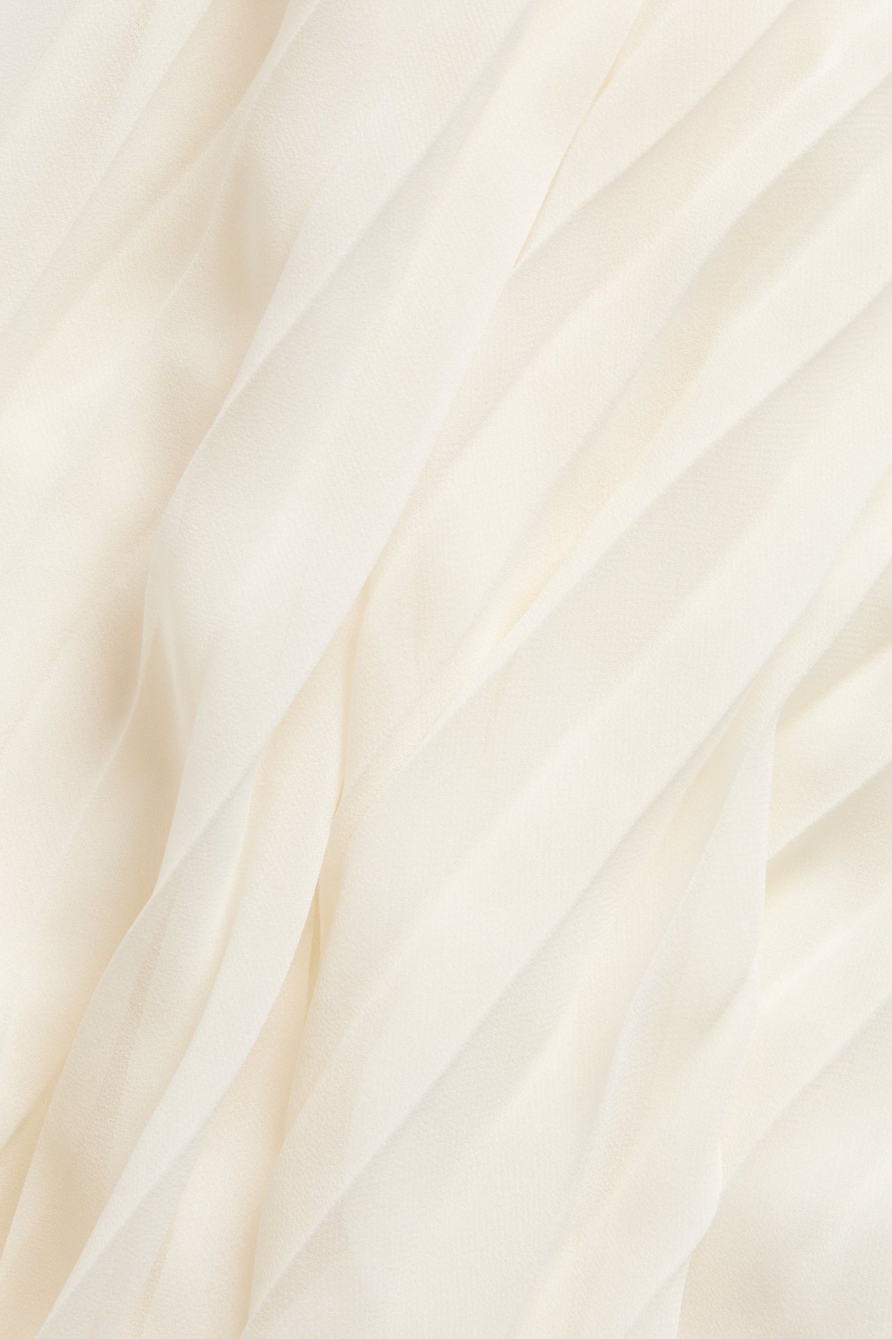 Närbild av en offwhite plisserad långkjols tyg, som visar dess enfärgade yta och mjuka veck.
