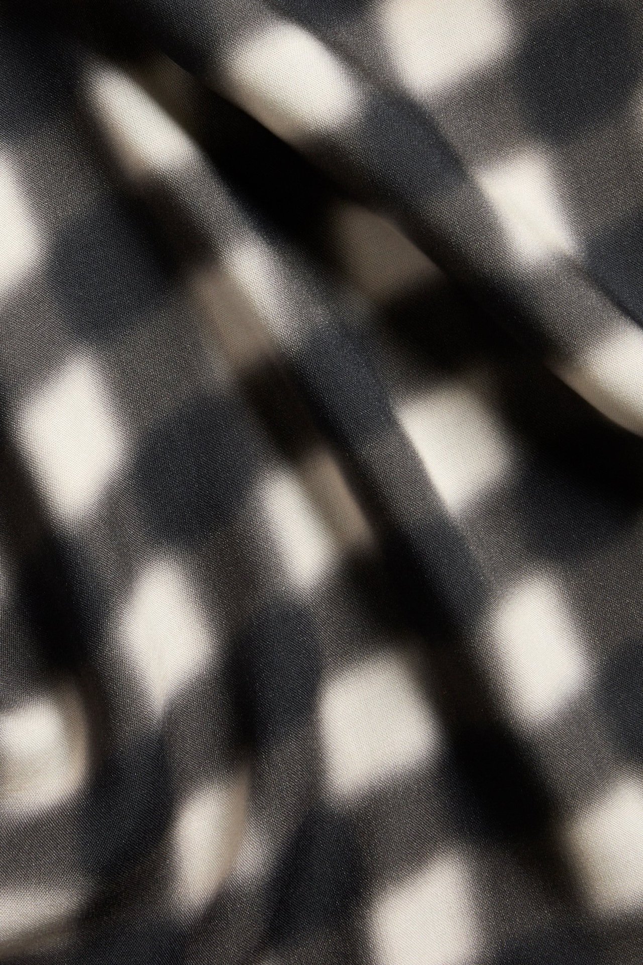 Lähikuva pehmeästä mustasta ja luonnonvalkoisesta sumeasta ruudullisesta viskoosikankaasta, osa pitkää hametta.