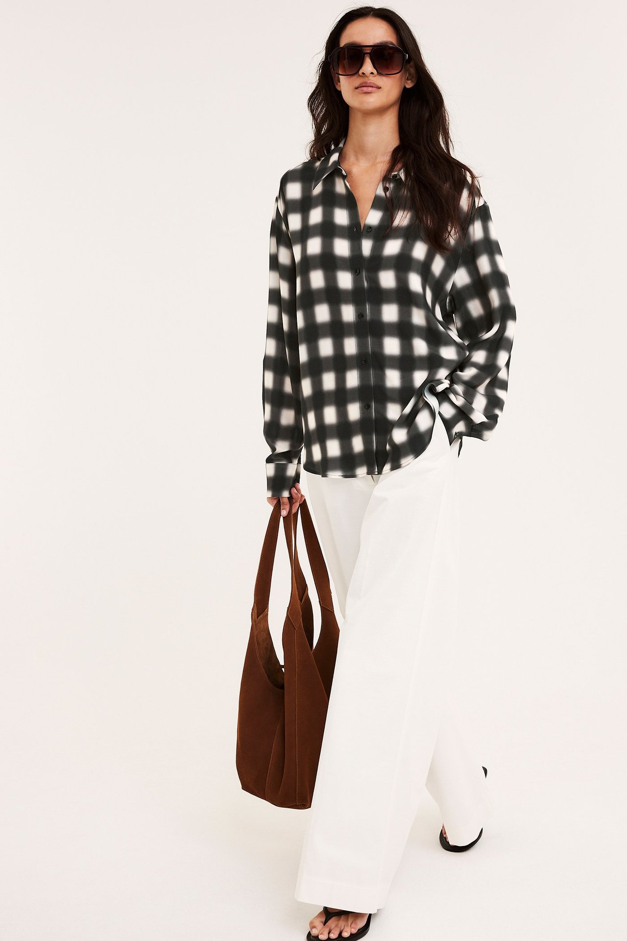 Edestä: Nainen löysässä mustavalkoruudullisessa viskoosipaidassa, valkoisissa leveissä housuissa, pitää ruskeaa laukkua.