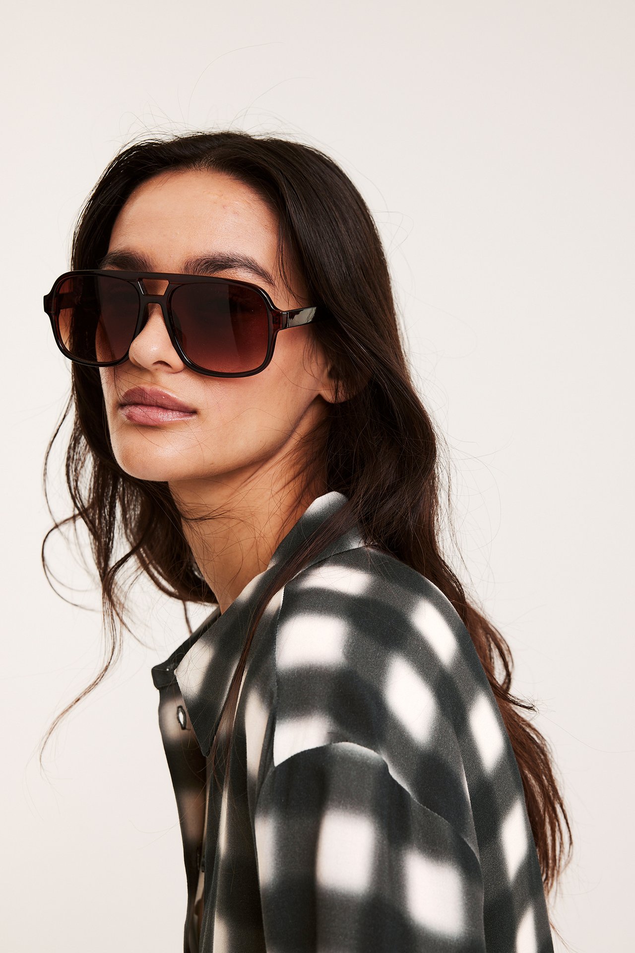 Närbild på en kvinna i svart- och vitrutig viskosskjorta och mörkbruna pilotglasögon.